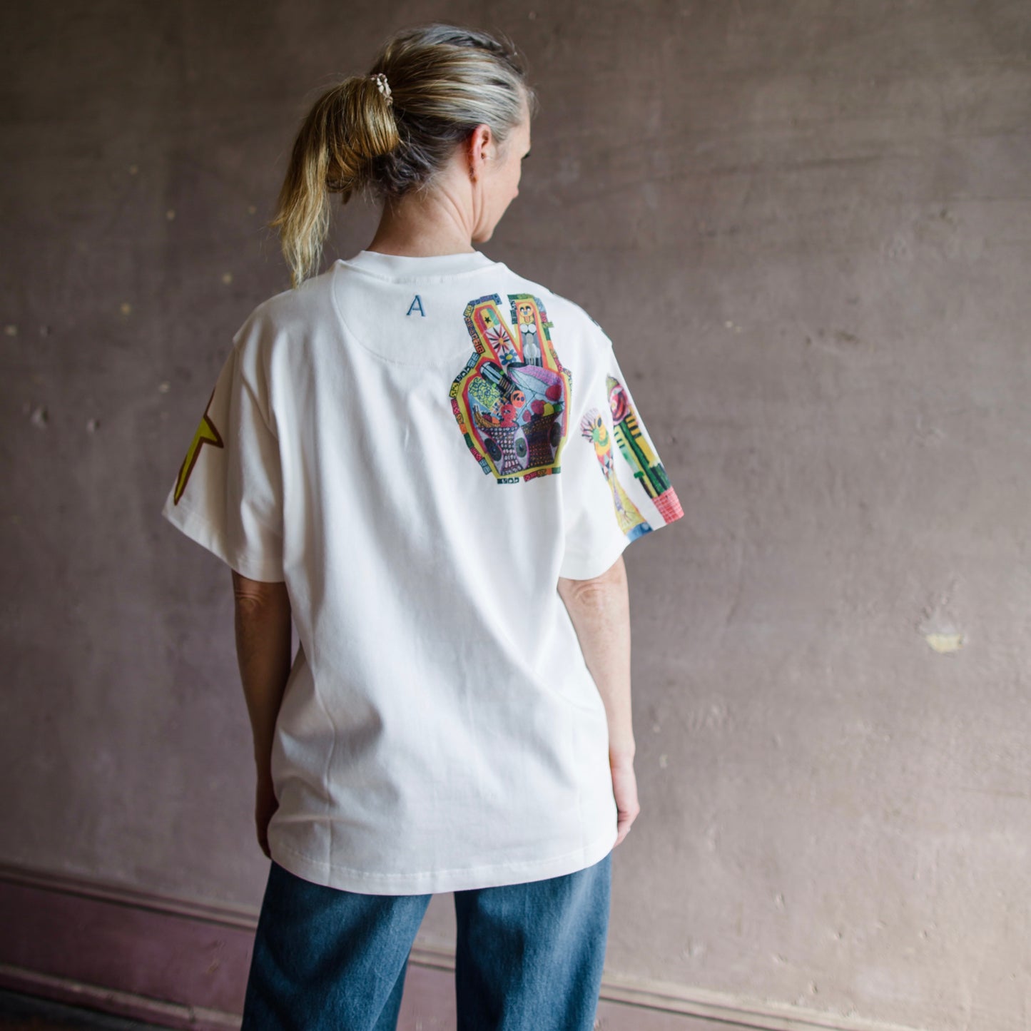 Image featuring a woman wearing the white Alemais T-shirt with Michael Swaney artwork on a relaxed fit and a ribbed neck detail in organic cotton.