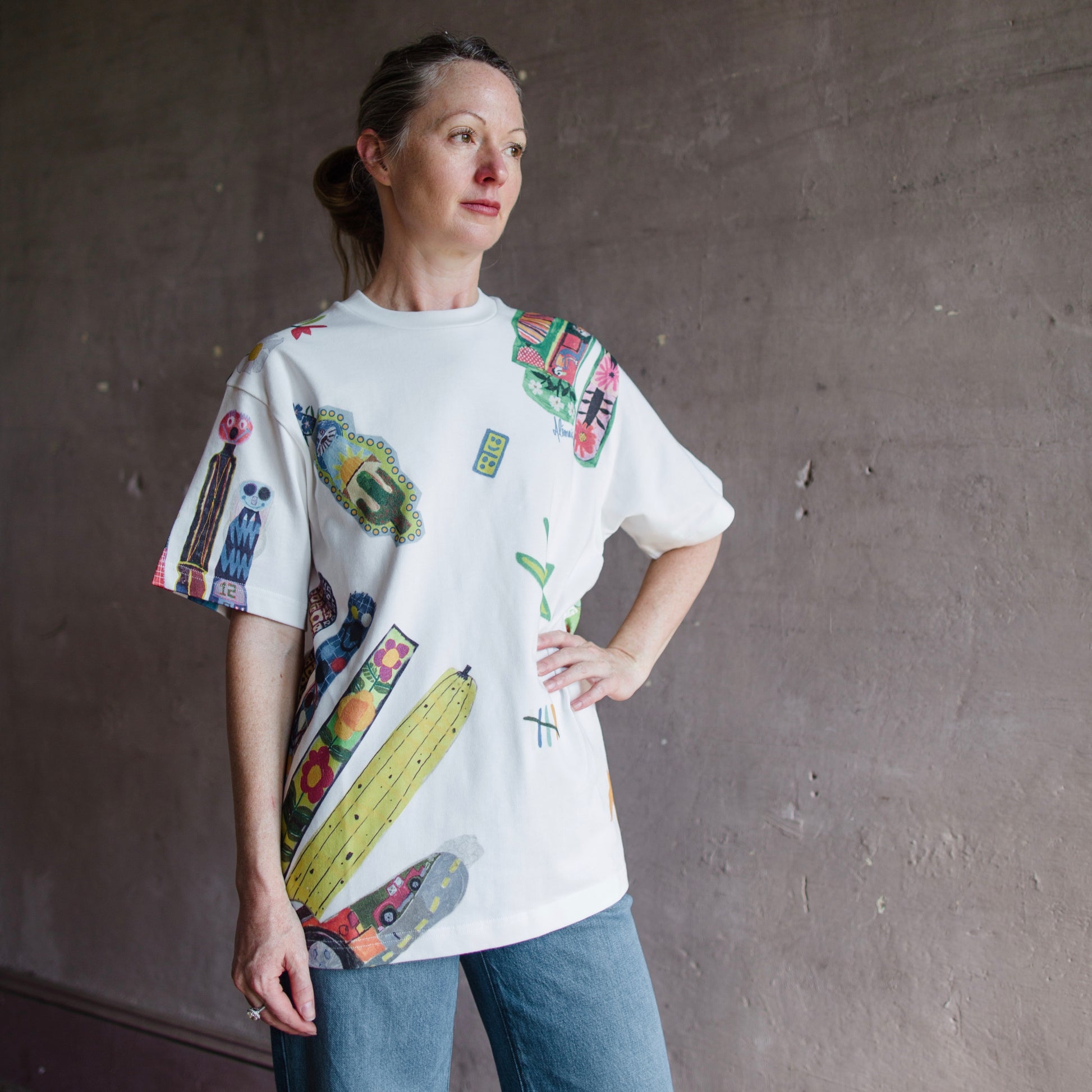 Image featuring a woman wearing the white Alemais T-shirt with Michael Swaney artwork on a relaxed fit and a ribbed neck detail in organic cotton.