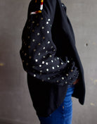 Image featuring a woman wearing the Alix of Bohemia Kiki Stardust button front black shirt with red, white, yellow, & black embroidery and metal discs on the  long sleeves.