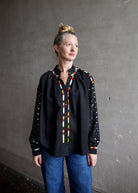 Image featuring a woman wearing the Alix of Bohemia Kiki Stardust button front black shirt with red, white, yellow, & black embroidery and metal discs on the  long sleeves.