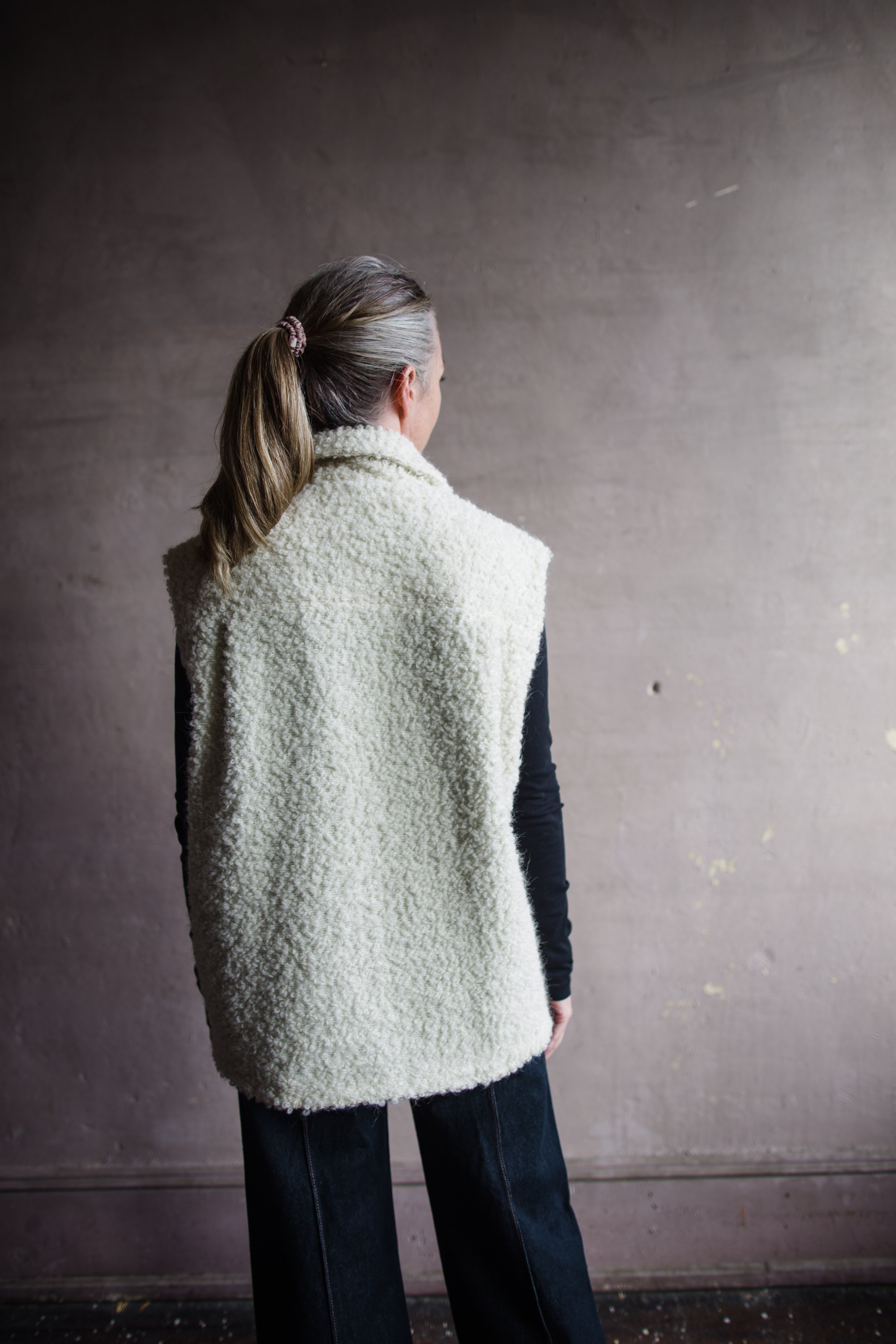 Image featuring a woman wearing the Alix of Bohemia Mickey Suri wool vest knitted with Italian alpaca wool in cream with front pockets with flaps and integral side seam pockets.