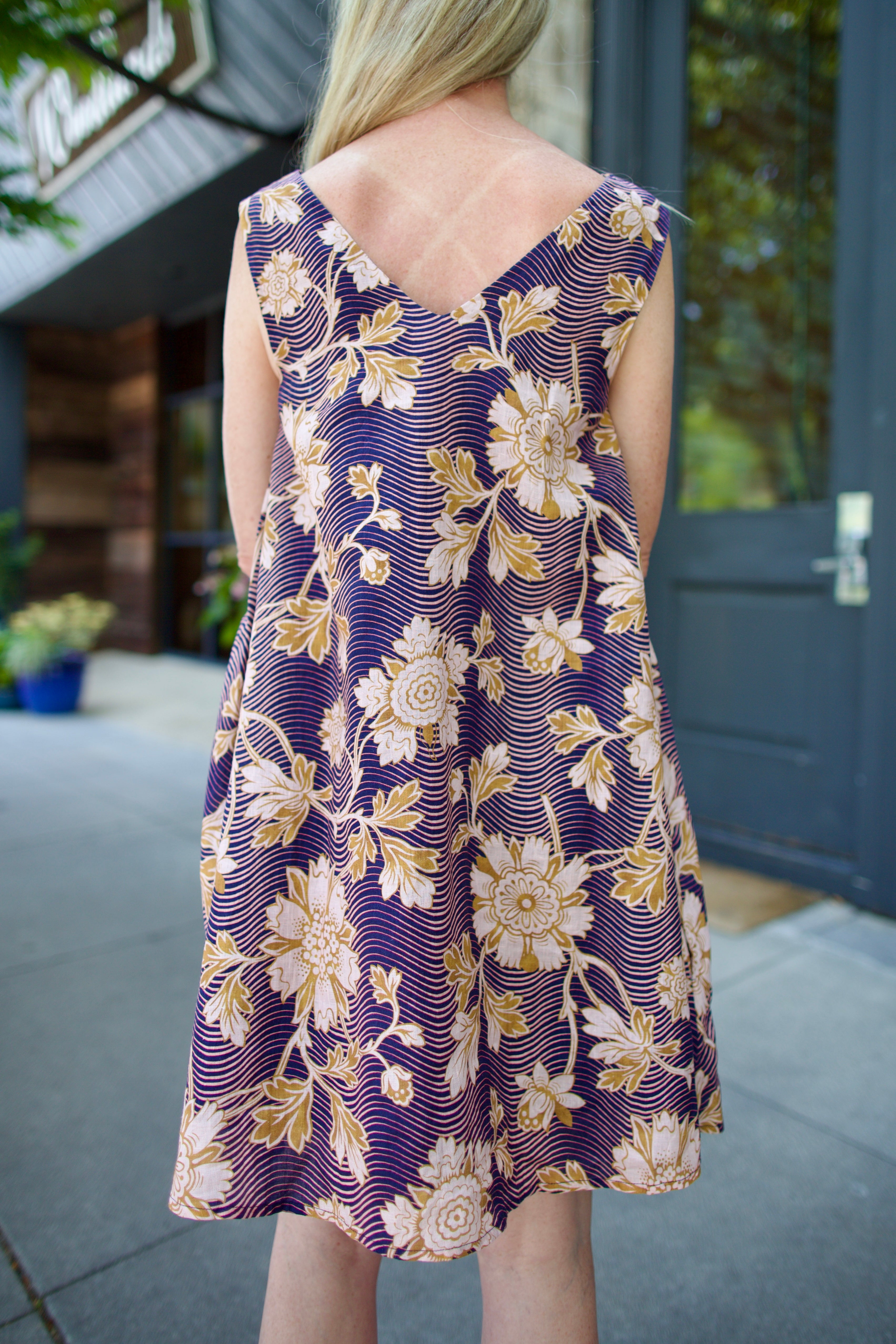 Model wearing a navy linen floral dress by high- end designer Alix of Bohemia Soleil Way Zinnia with v-neck and pockets