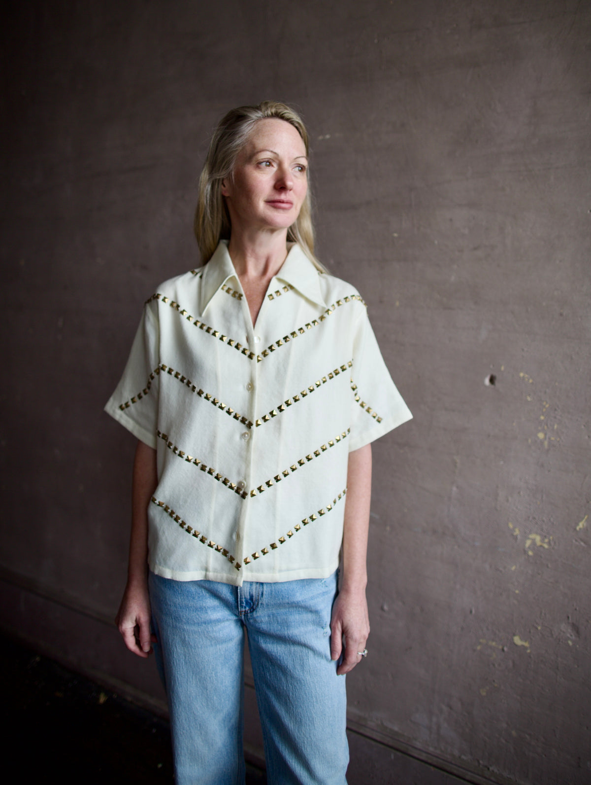 Mature woman wearing Alix of Bohemia Stevie Studded top with button front short sleeves and a collar metal embellishments in V design across entire front