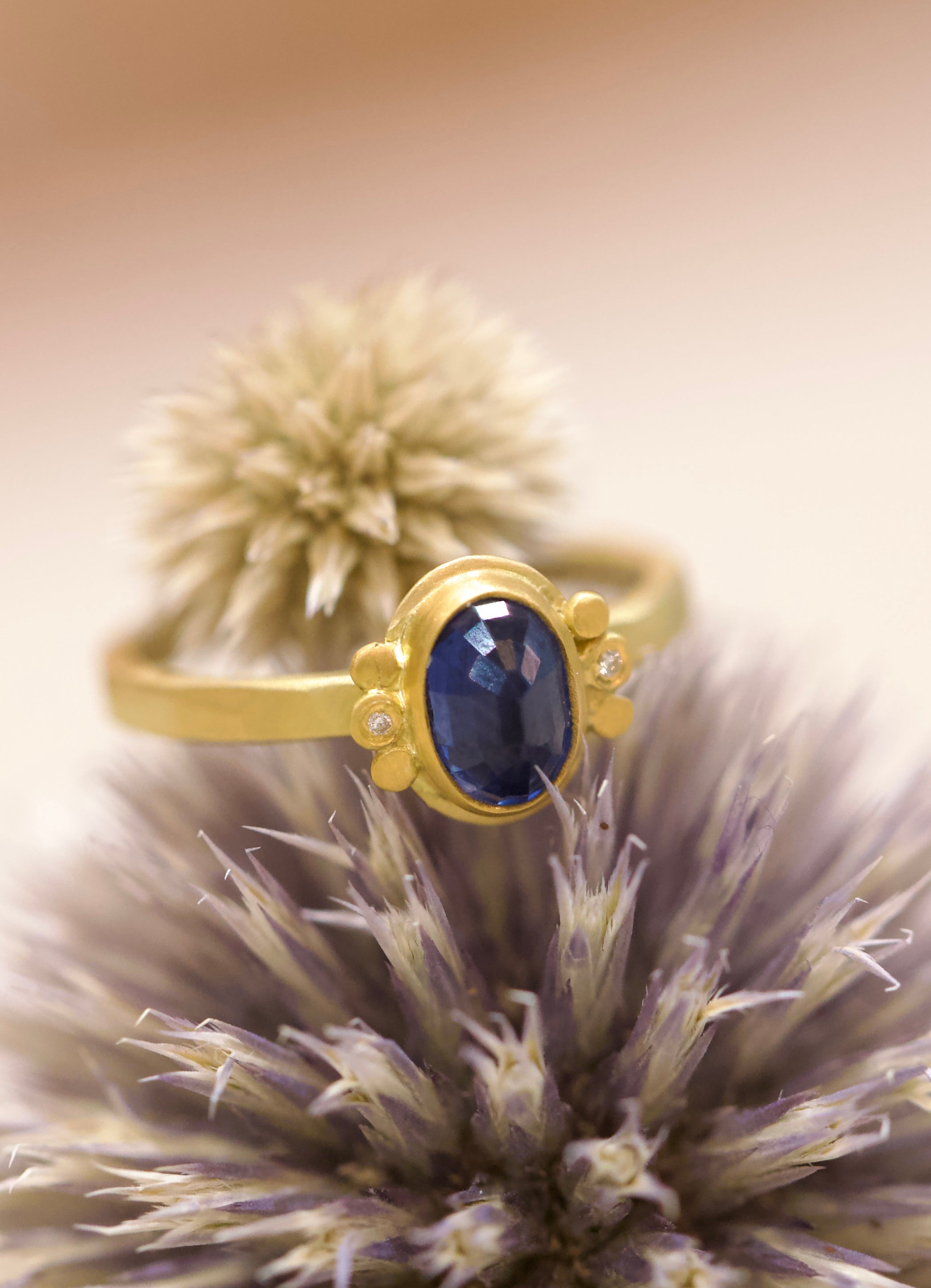 Image of handmade rosecut oval blue sapphire ring by Ananda Khalsa designed with a 22kt gold bezel, 18kt gold band, and 22kt gold diamond trios.