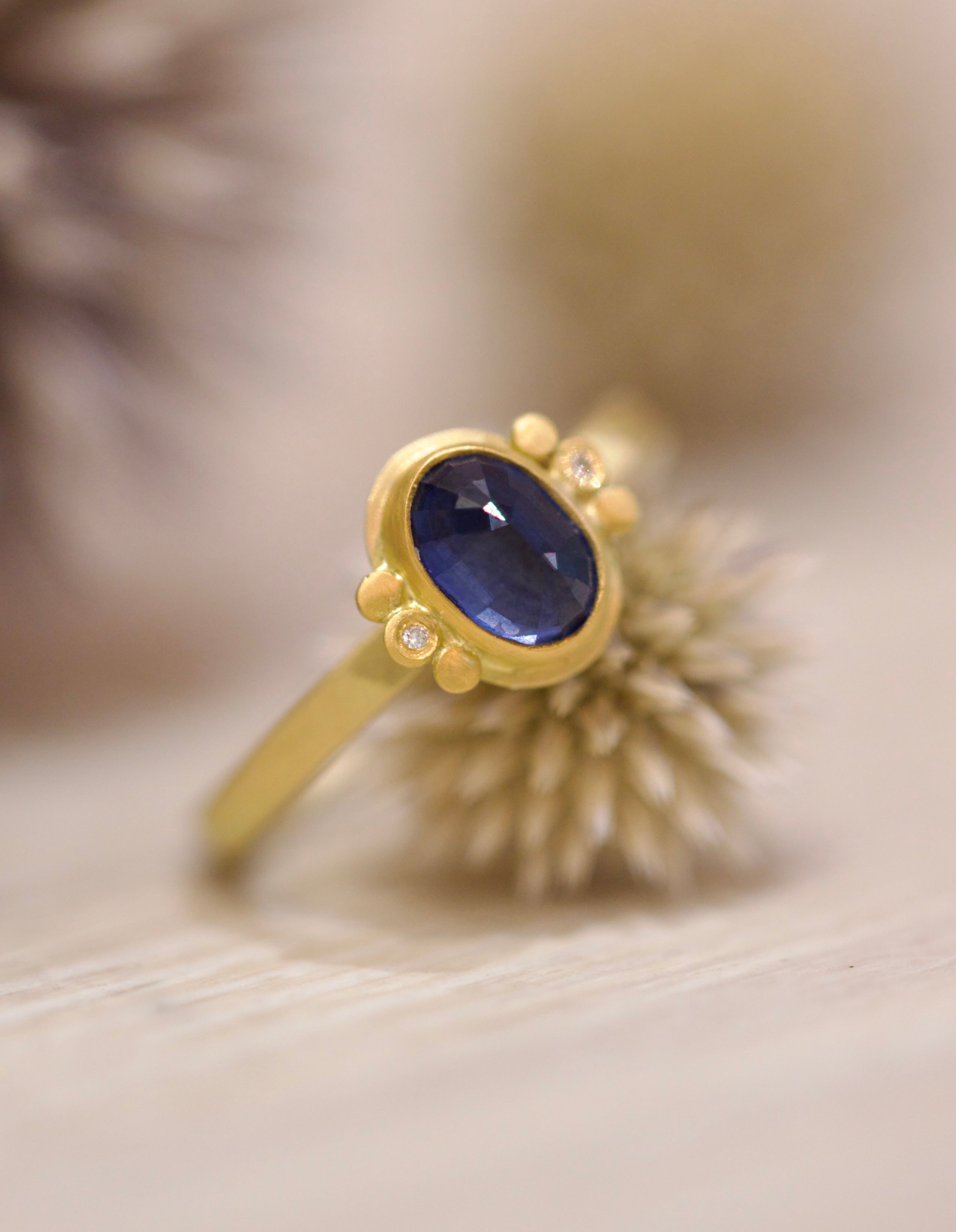 Image of handmade rosecut oval blue sapphire ring by Ananda Khalsa designed with a 22kt gold bezel, 18kt gold band, and 22kt gold diamond trios.