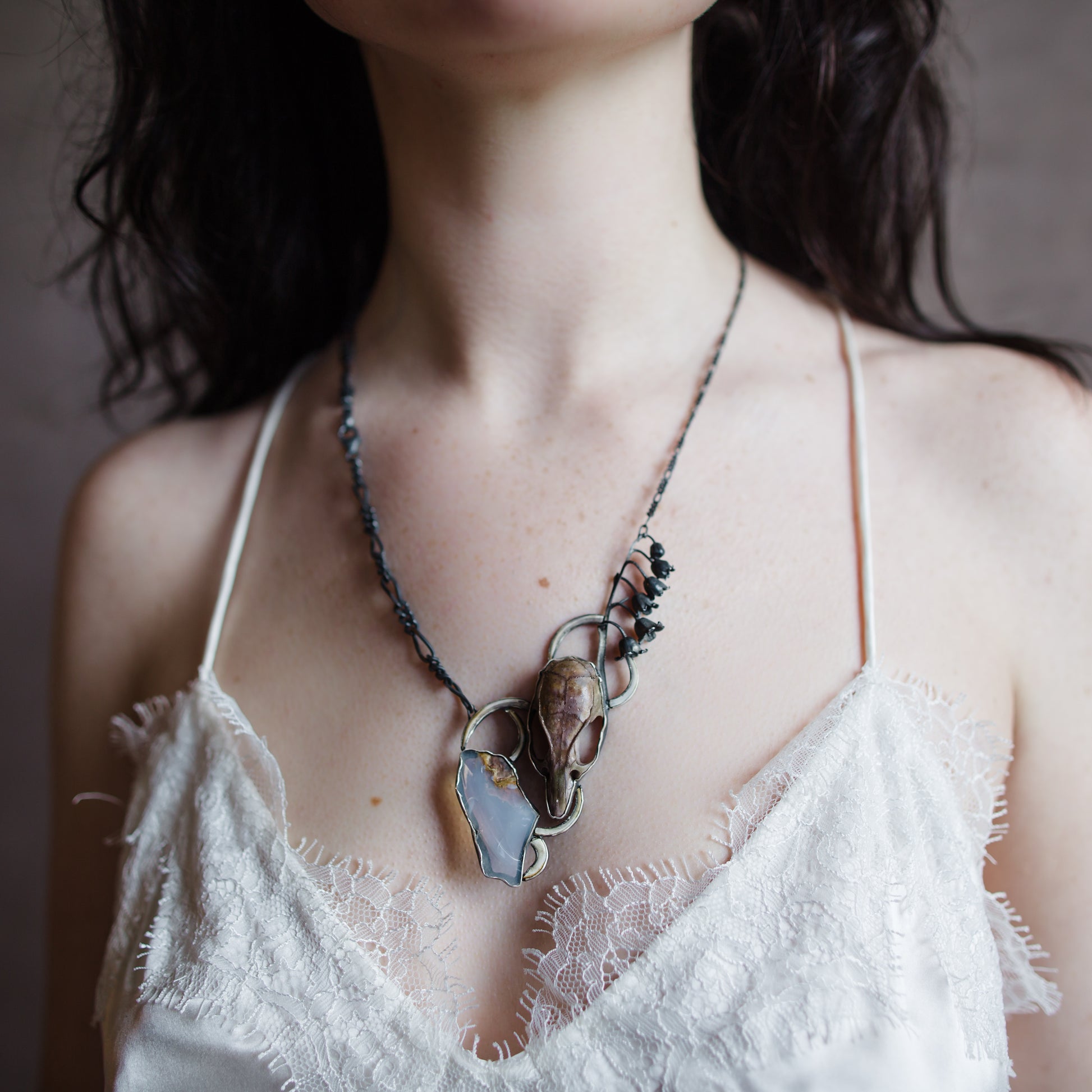 Image featuring a woman wearing North Carolina artist Anna Johnson Inciroda Necklace with Rat skull, rodent incisors, Oregon opal, silver and lily of the valley casting