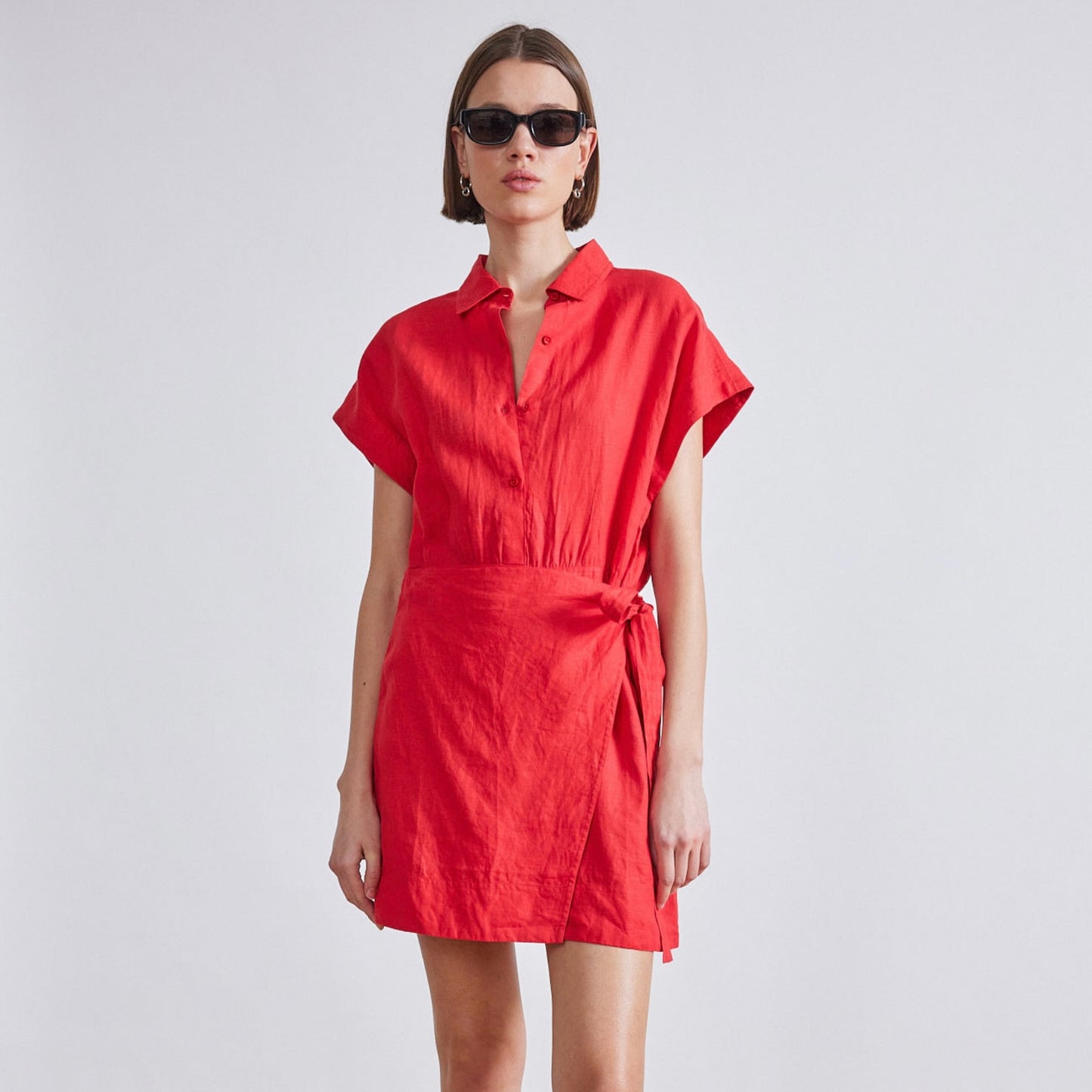 Image featuring a woman wearing the red Catania classic shirting dress from Apiece Apart with a self tie waist, relaxed bodice, dolman sleeve, shirt collar neckline and button placket.