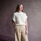 Image featuring a woman wearing the Oliva linen sweater by Apiece Apart with a wide crewneck collar, drop shoulder and ribbed details throughout in cream.