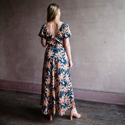 Image featuring a woman wearing the silk Monet maxi dress by Apiece Apart with feminine flutter sleeves, fitted waist, V neck, full A-line skirt, and zipper closure at left side.