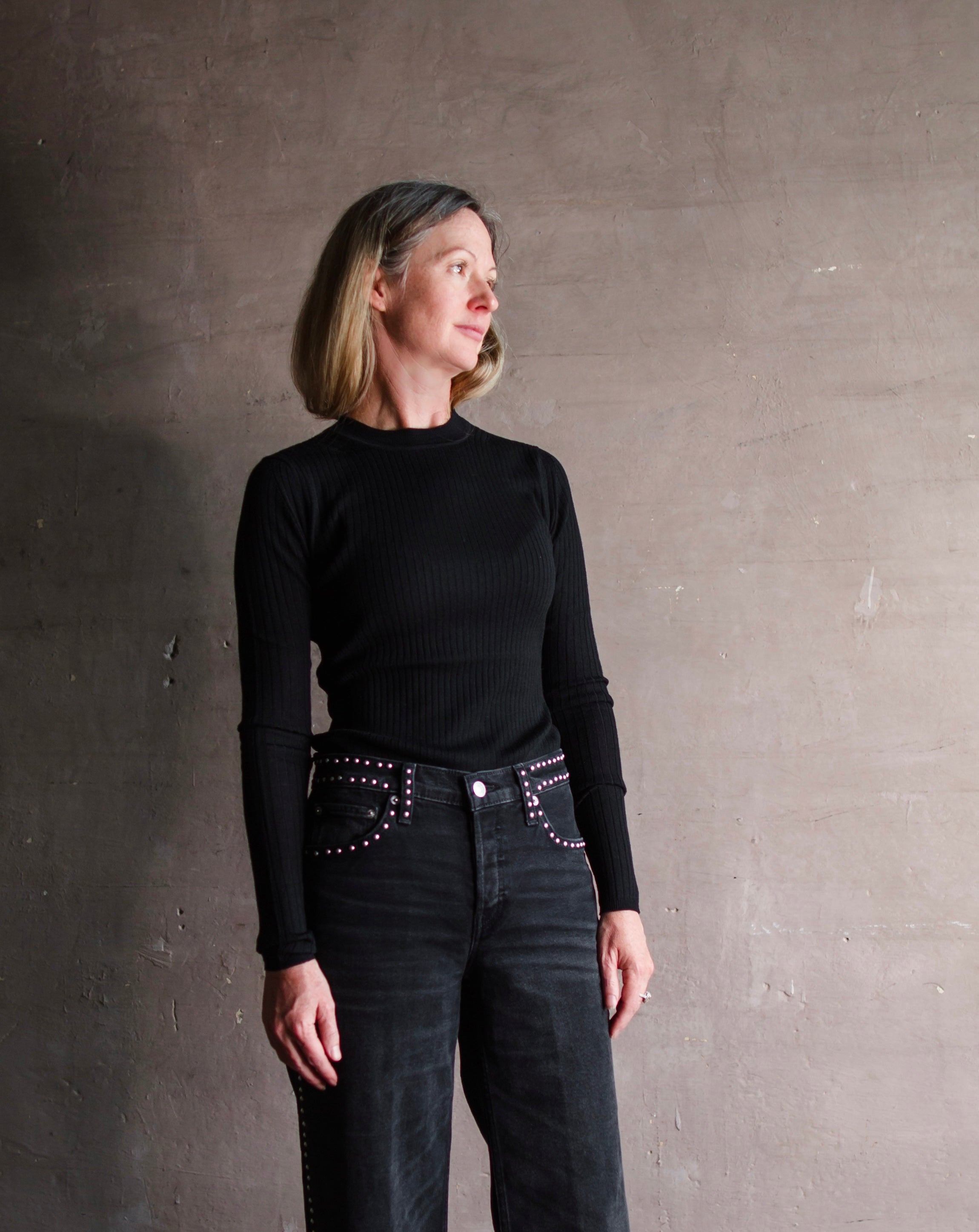 Image featuring a woman wearing the sweater top by Apiece Apart merino wool with a crew neckline, ribbed texture and a tailored fit in black