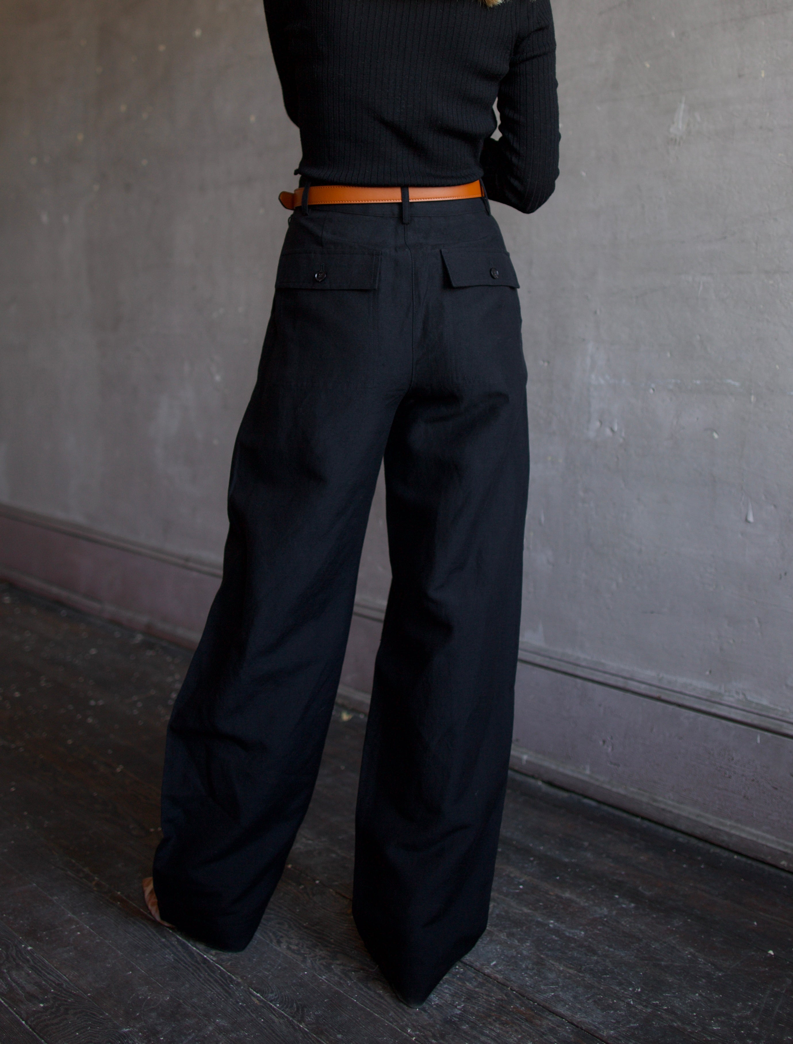 image of the back of a woman wearing the Apiece Apart merino ribbed sweater and mirabelle trousers with the Ulla Johnson gia belt