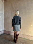 Mature woman stands with her back to the camera wearing a gray textured Marta mini skirt from Apiece Apart with brown knee-high leather boots perfect for Fall
