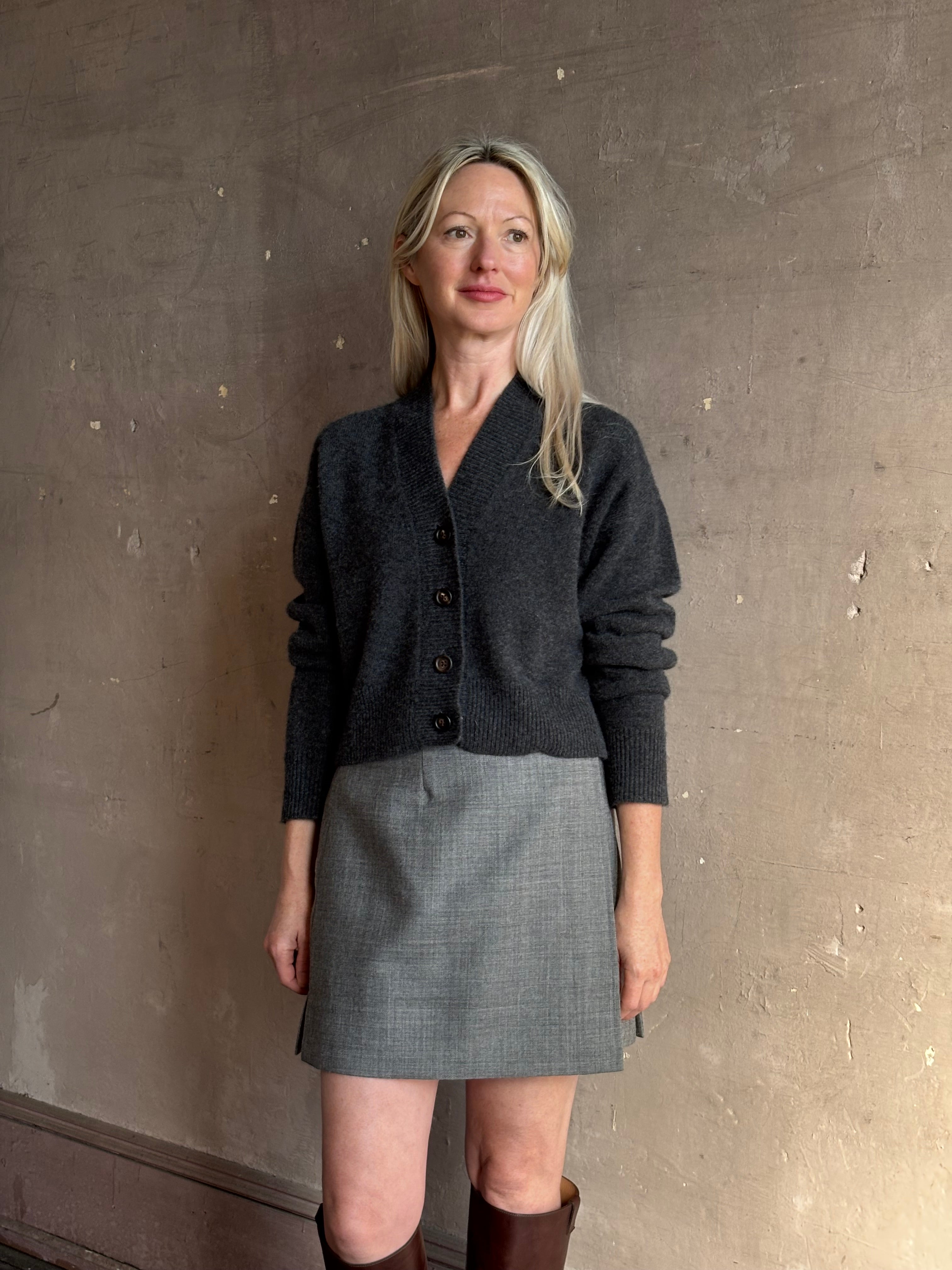 Close up image of mature woman wearing a dark charcoal gray button-up cardigan and Apiece Apart Marta grey virgin wool mini skirt