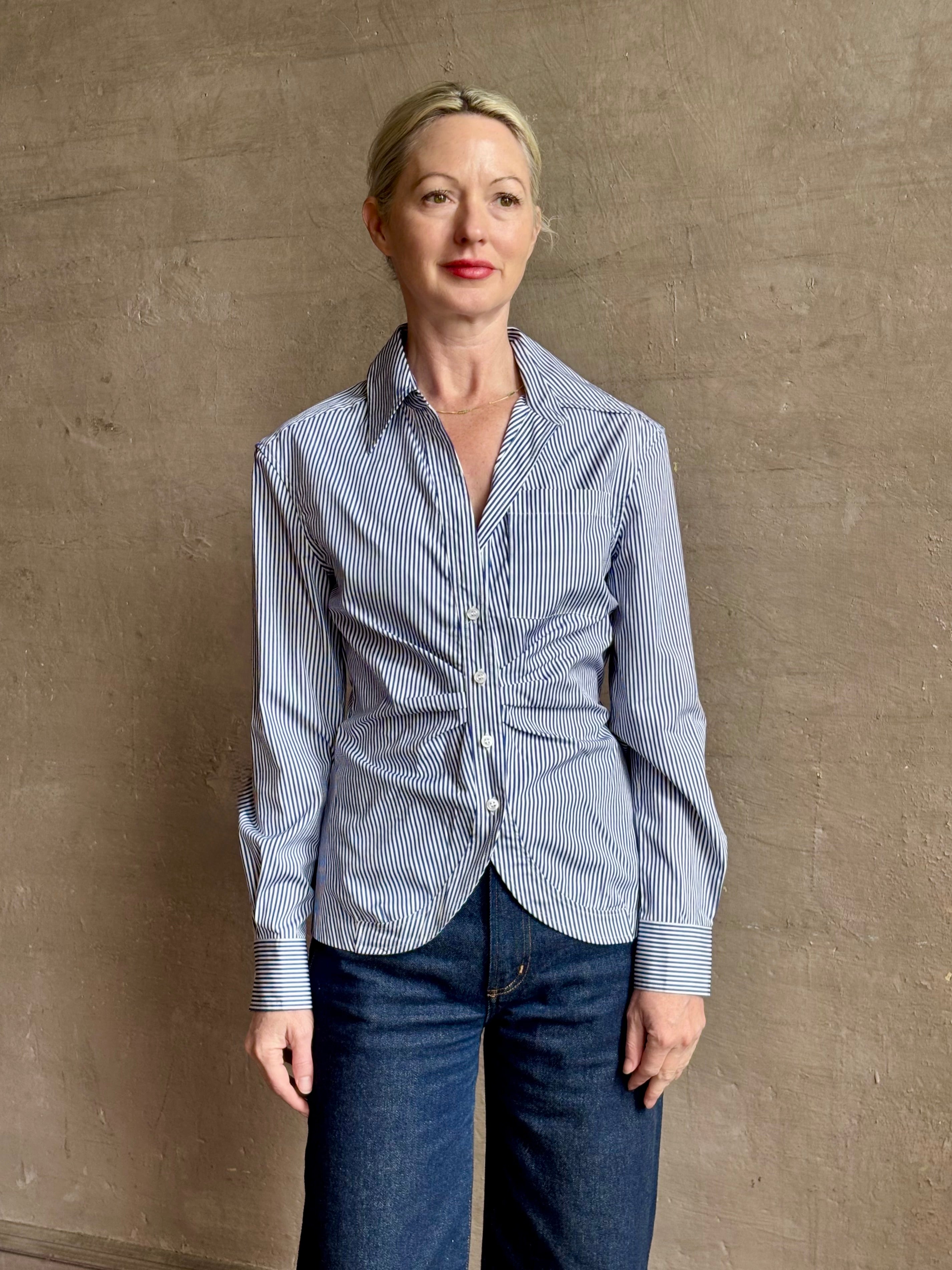 Mature woman wearing the European tailored Sierra Shirt from Callas rendered in a crisp navy and white stripe and crafted from cotton poplin featuring a flattering ruched front , long sleeves, v-neck and rounded bottom detail
