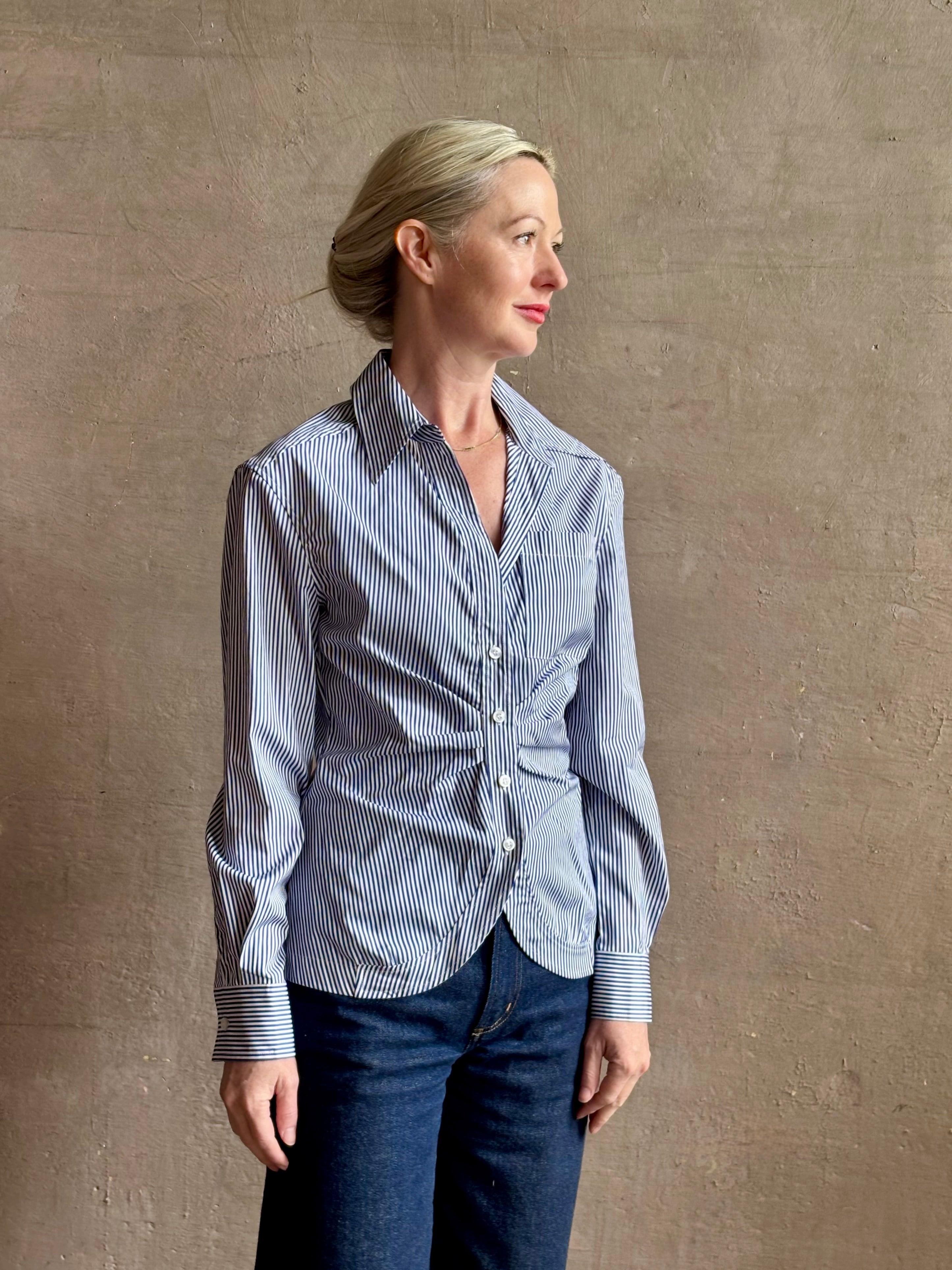 Mature woman wearing the European tailored Sierra Shirt from Callas rendered in a crisp navy and white stripe and crafted from cotton poplin featuring a flattering ruched front , long sleeves, v-neck and rounded bottom detail
