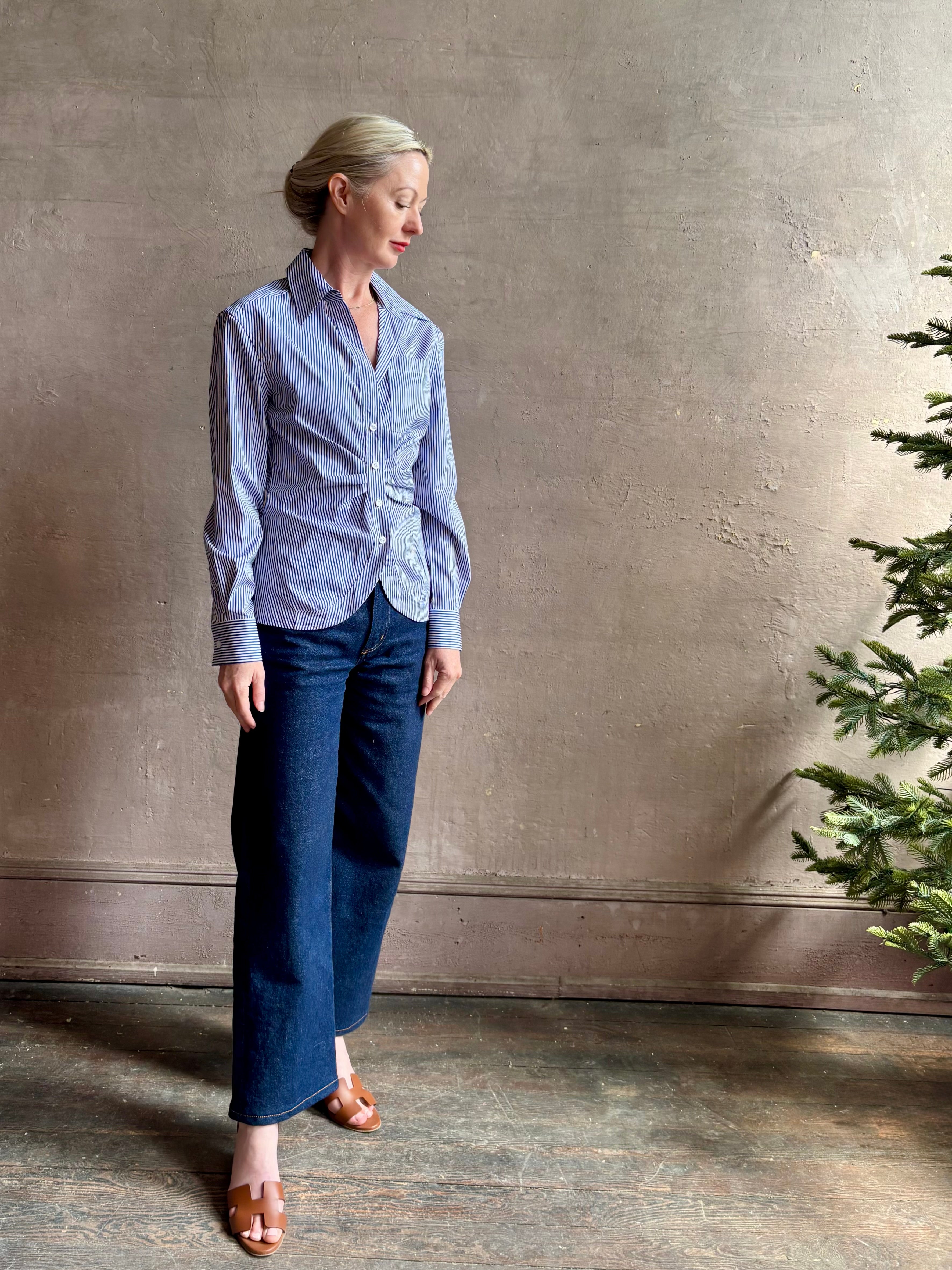 Mature woman wearing the European tailored Sierra Shirt from Callas rendered in a crisp navy and white stripe and crafted from cotton poplin featuring a flattering ruched front , long sleeves, v-neck and rounded bottom detail