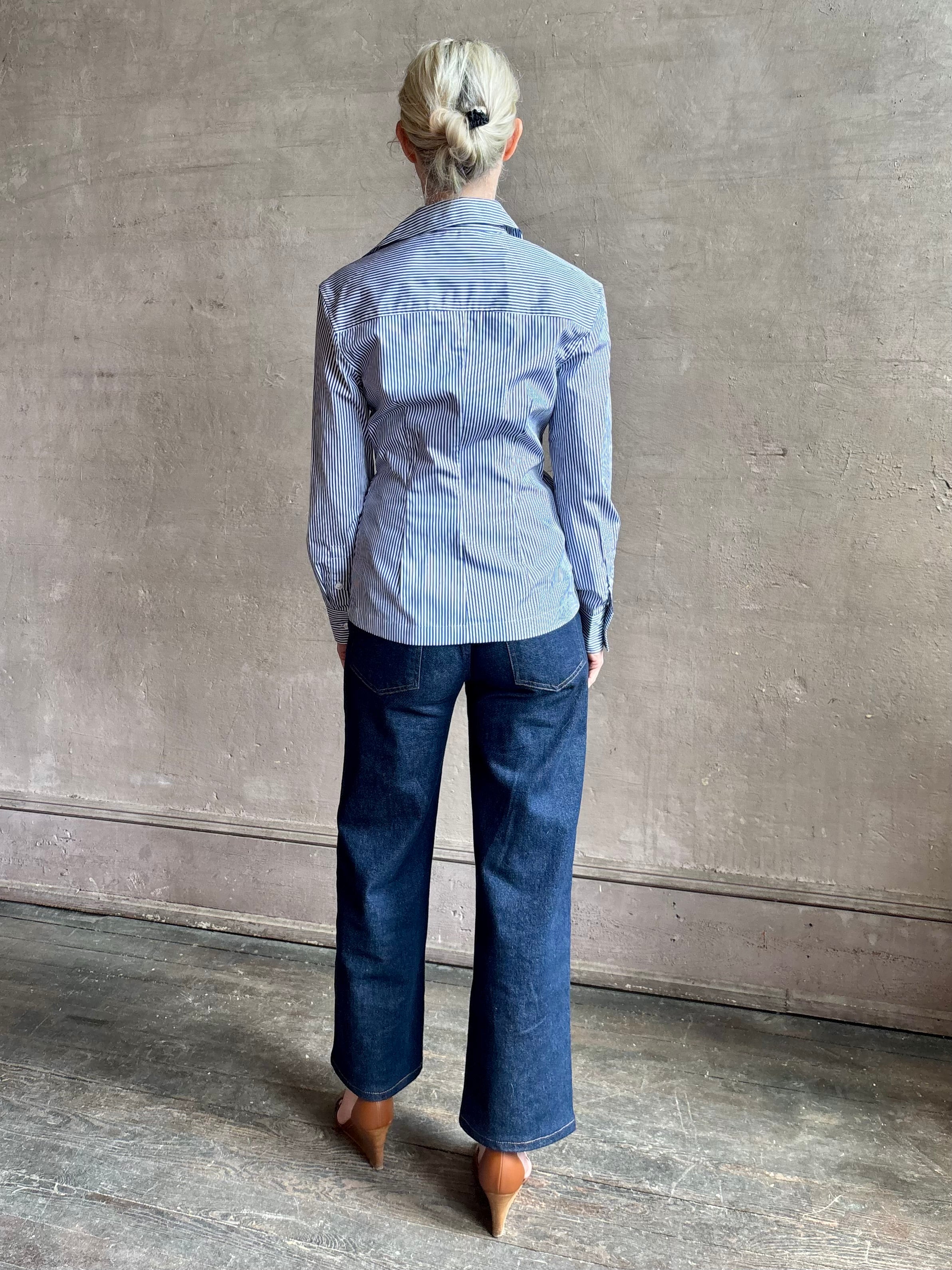 Mature woman wearing the European tailored Sierra Shirt from Callas rendered in a crisp navy and white stripe and crafted from cotton poplin featuring a flattering ruched front , long sleeves, v-neck and rounded bottom detail