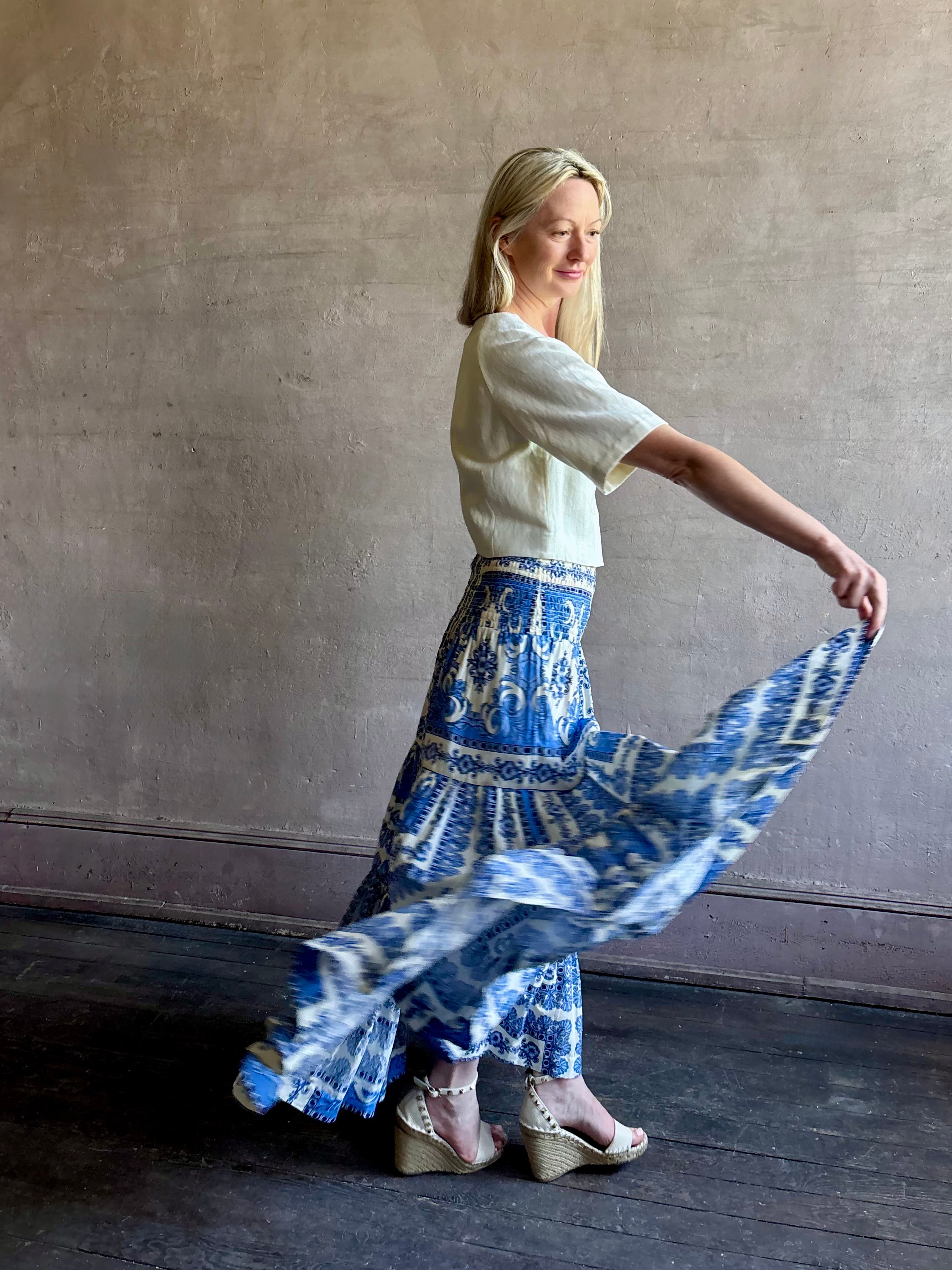 Mature woman wearing Emilia Skirt from Cara Cara rendered in the Hudson Scarf Sky blue and white print crafted from 100% cotton with shirred drop waist and ruffled tiered full skirt