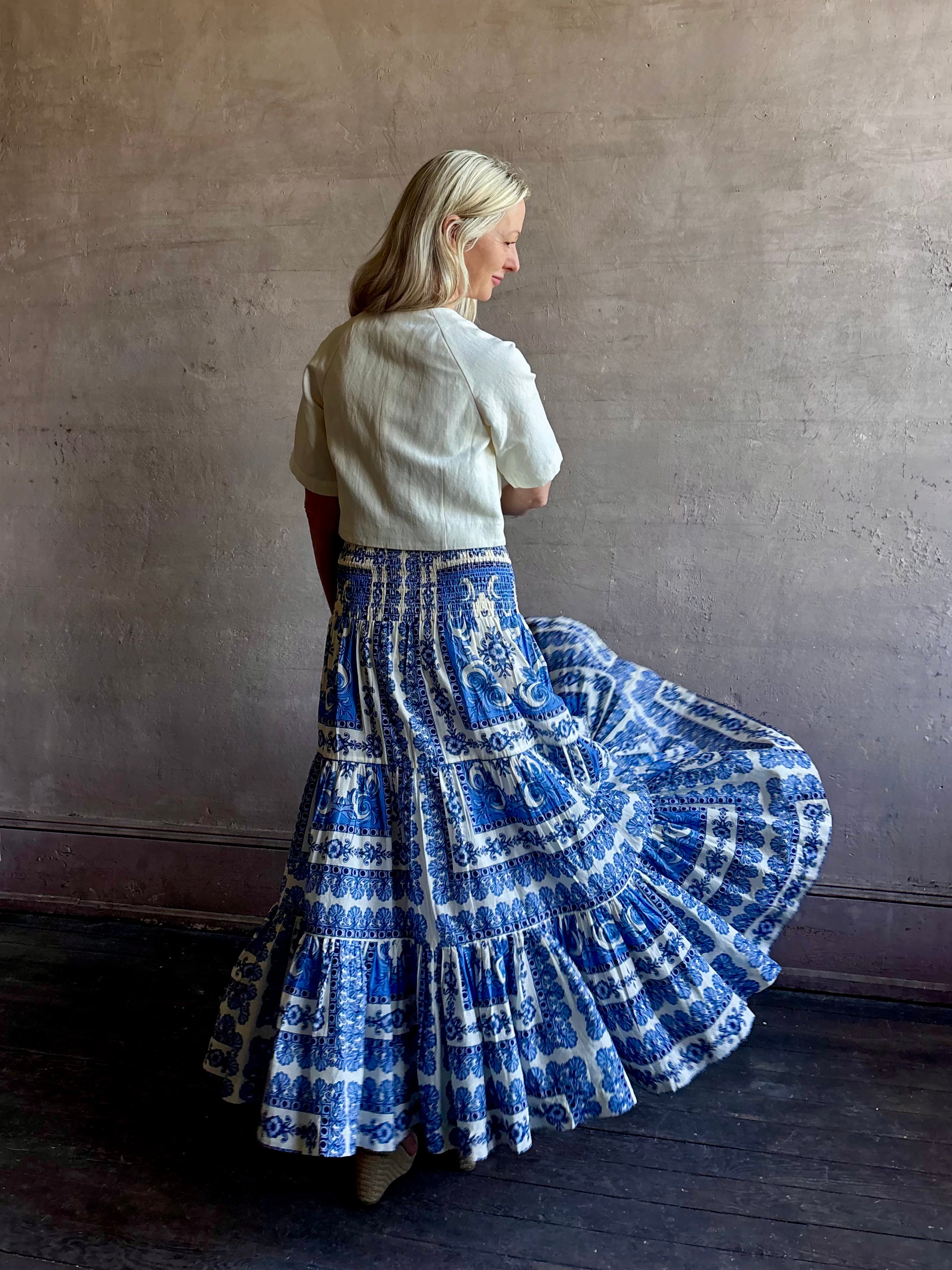 Mature woman wearing Emilia Skirt from Cara Cara rendered in the Hudson Scarf Sky blue and white print crafted from 100% cotton with shirred drop waist and ruffled tiered full skirt