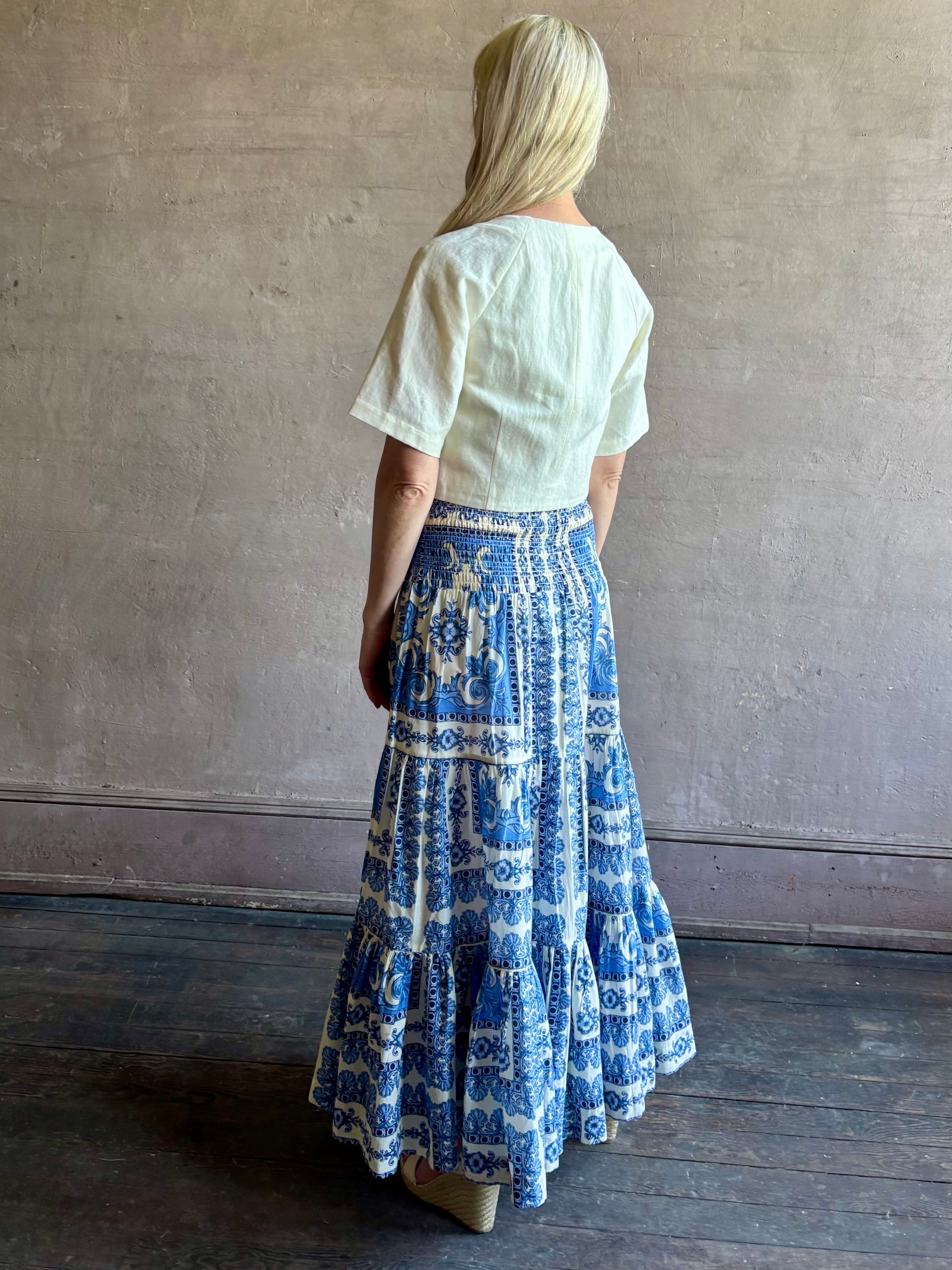 Mature woman wearing Emilia Skirt from Cara Cara rendered in the Hudson Scarf Sky blue and white print crafted from 100% cotton with shirred drop waist and ruffled tiered full skirt