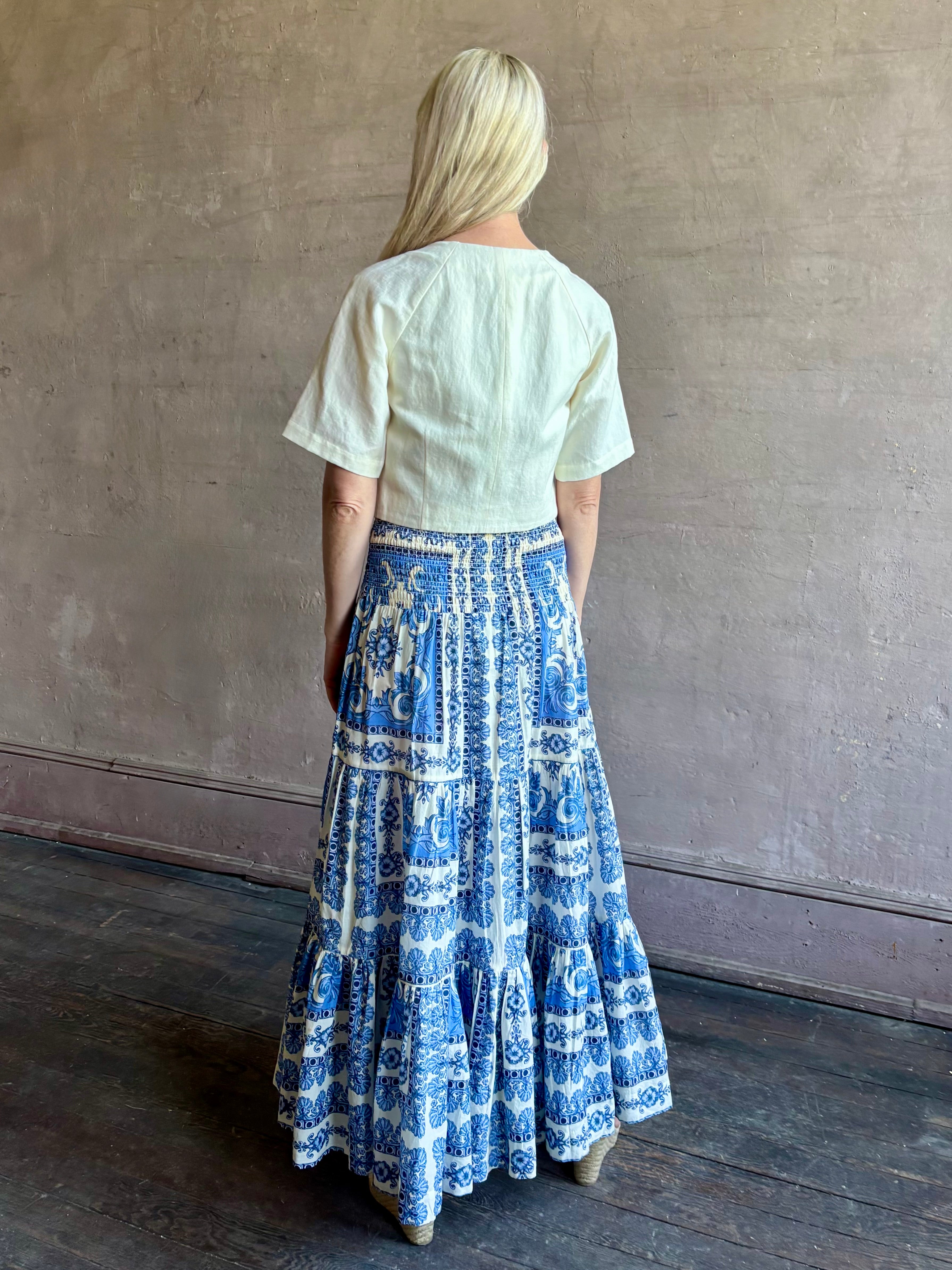 Mature woman wearing Emilia Skirt from Cara Cara rendered in the Hudson Scarf Sky blue and white print crafted from 100% cotton with shirred drop waist and ruffled tiered full skirt