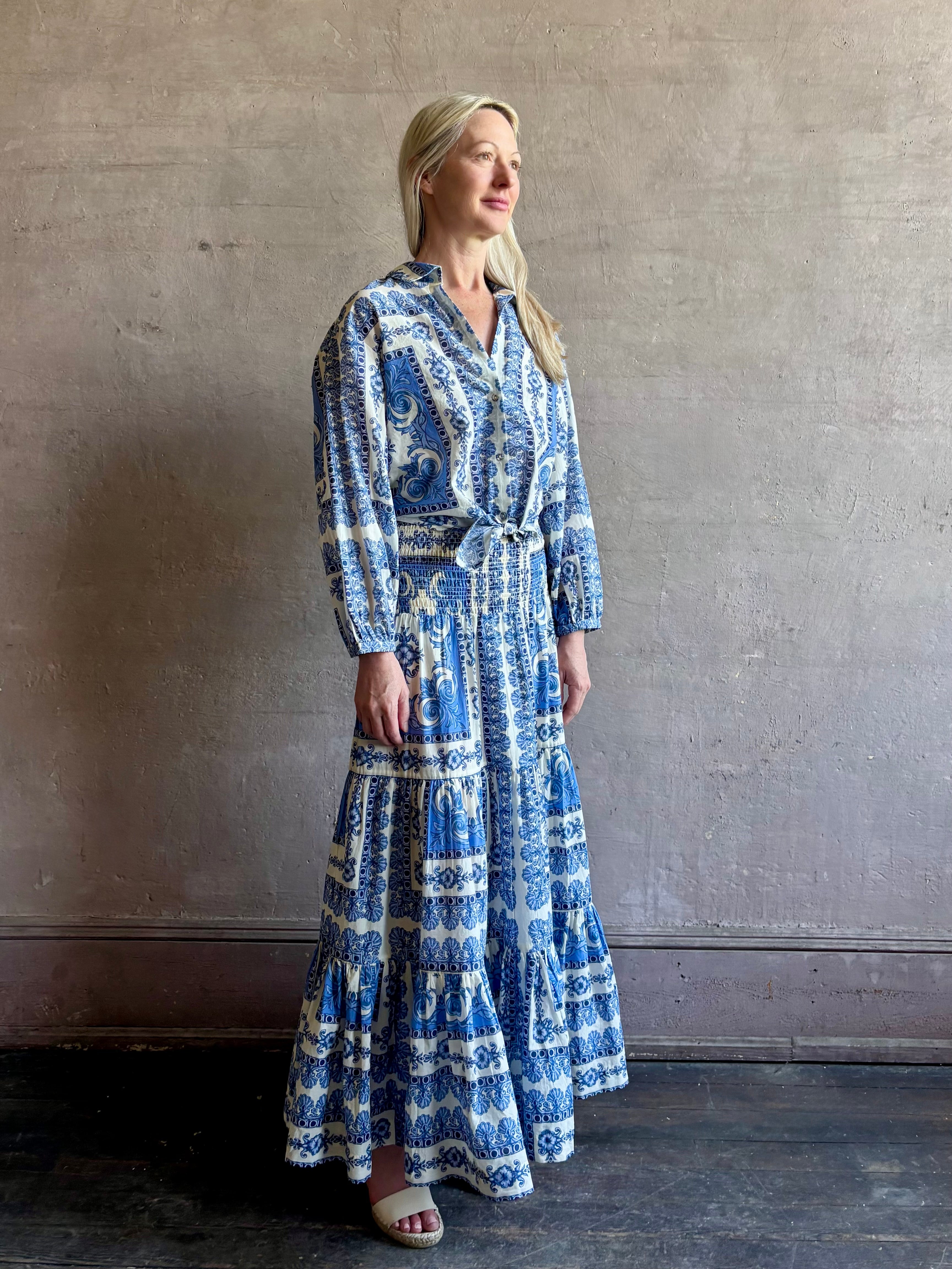 Mature woman wearing Emilia Skirt from Cara Cara rendered in the Hudson Scarf Sky blue and white print crafted from 100% cotton with shirred drop waist and ruffled tiered full skirt