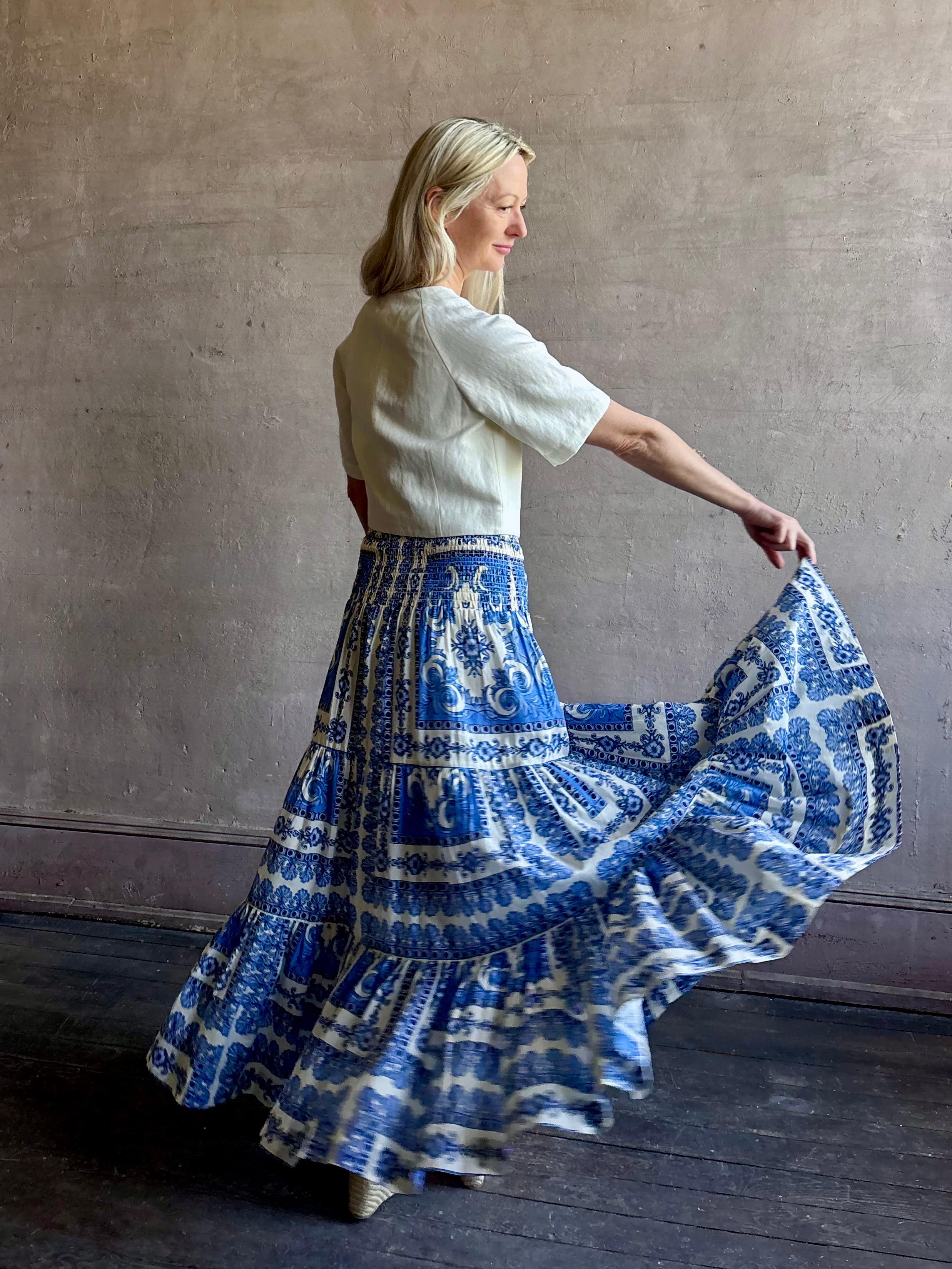 Mature woman wearing Emilia Skirt from Cara Cara rendered in the Hudson Scarf Sky blue and white print crafted from 100% cotton with shirred drop waist and ruffled tiered full skirt