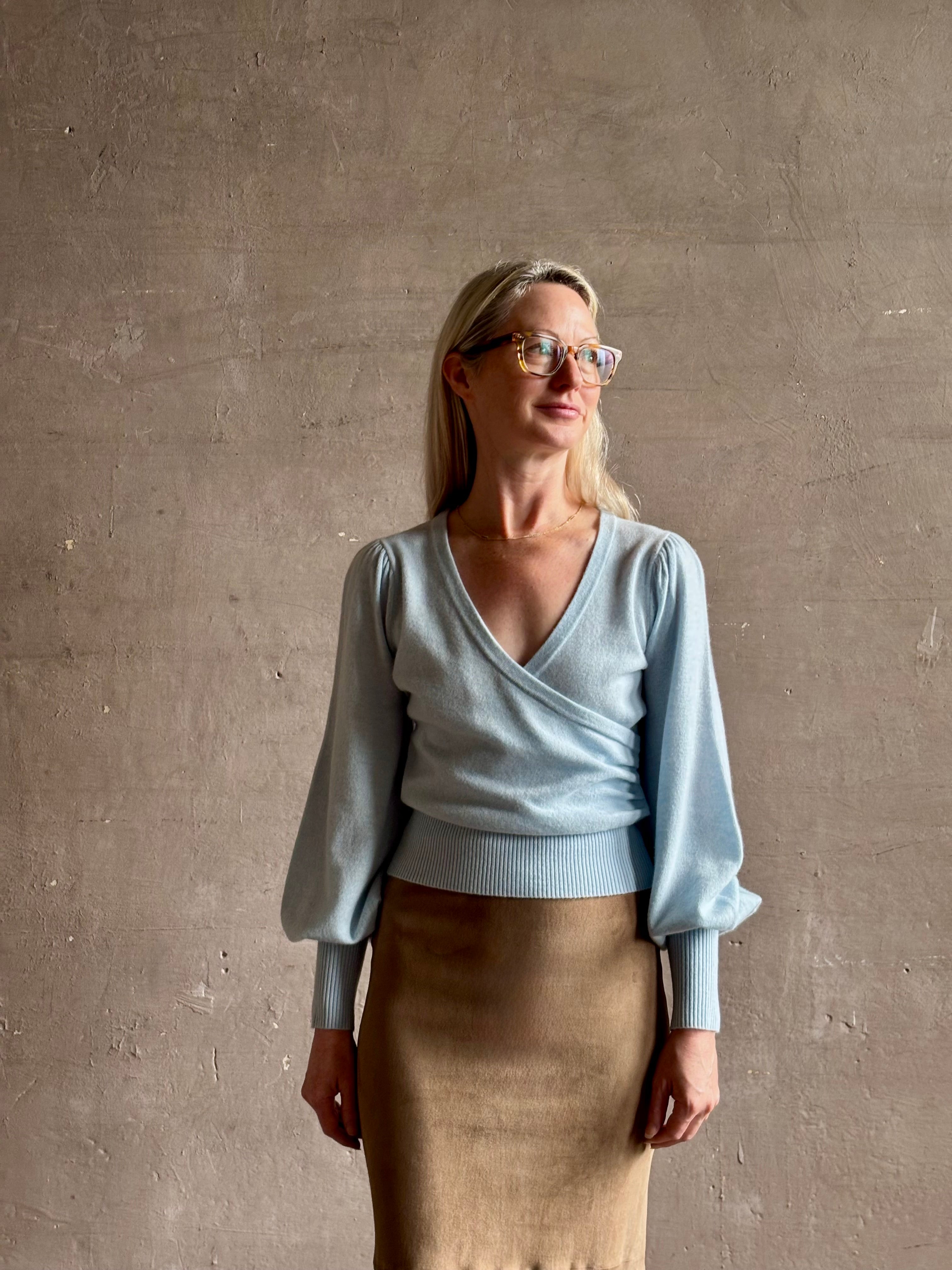 mature woman wearing designer Cara Cara wool-cashmere blend light blue wrap sweater v-neck and long sleeves