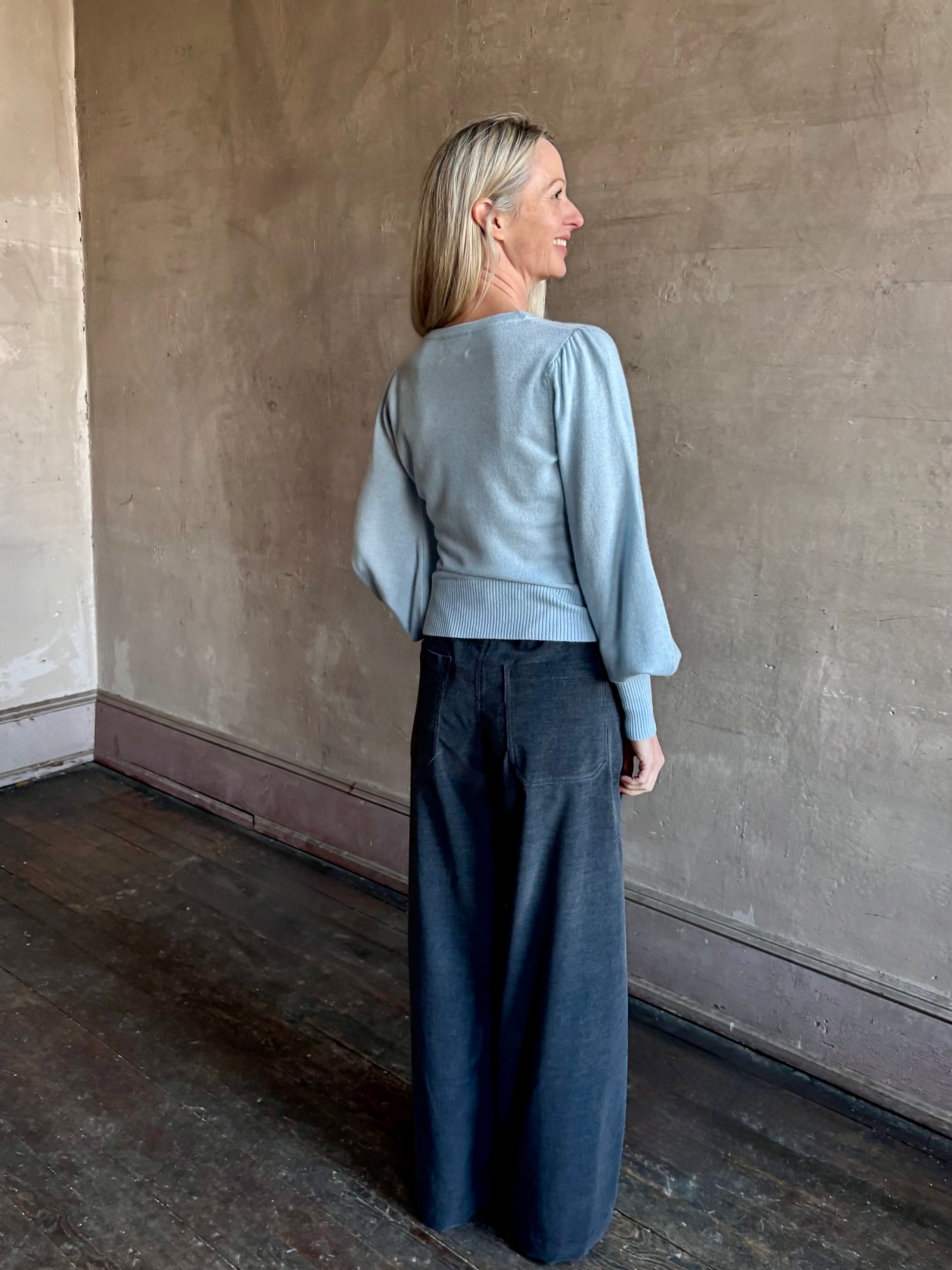 Back image of woman wearing designer Cara Cara wool-cashmere blend light blue wrap sweater with a v-neck and long sleeves