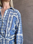 Mature woman wearing the Rumson Top from Cara Cara rendered in a blue and white Hudson Scarf Sky print and crafted from 100% cotton with long sleeves, button down v- neck and tie front cropped top