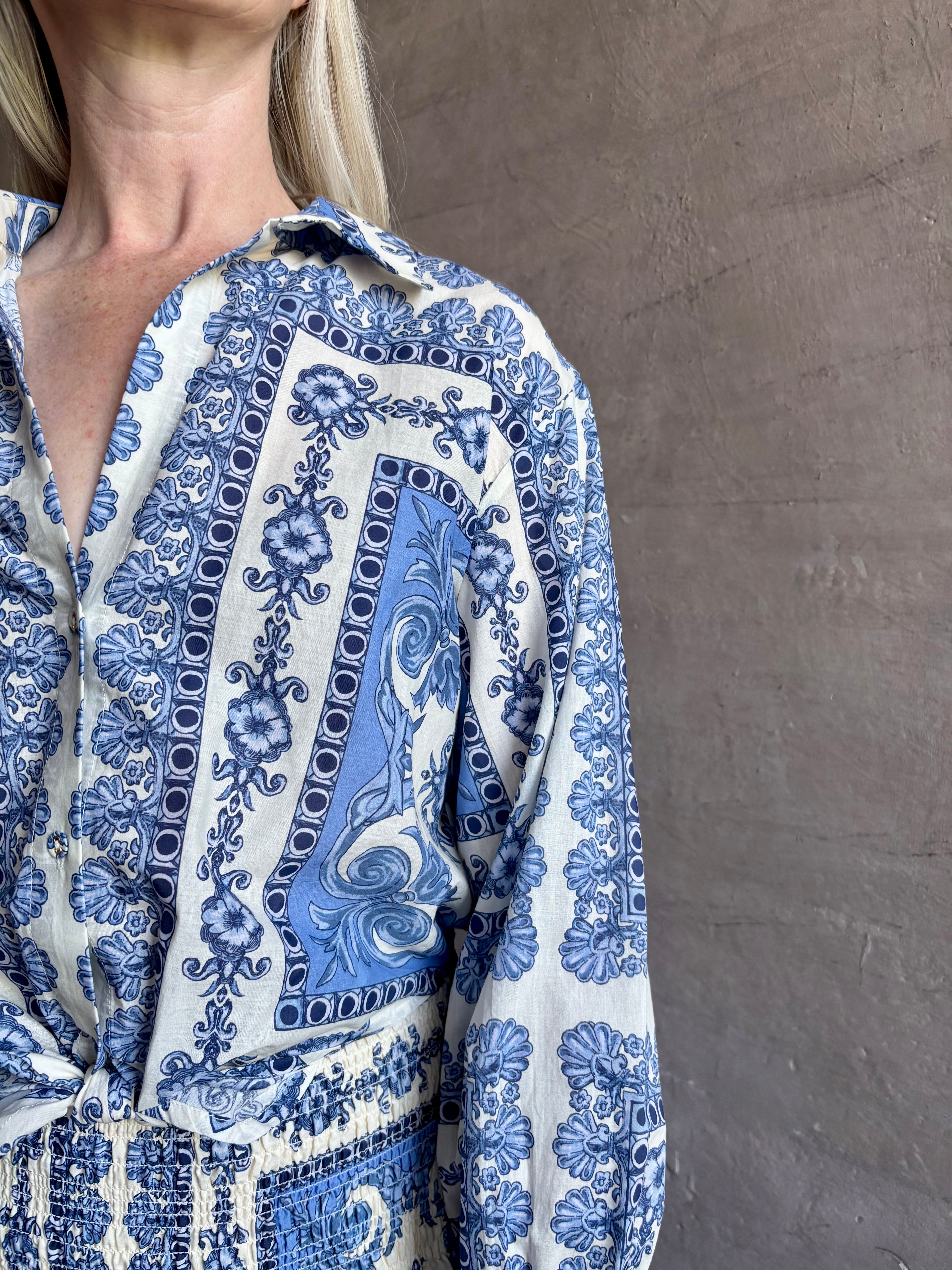 Mature woman wearing the Rumson Top from Cara Cara rendered in a blue and white Hudson Scarf Sky print and crafted from 100% cotton with long sleeves, button down v- neck and tie front cropped top