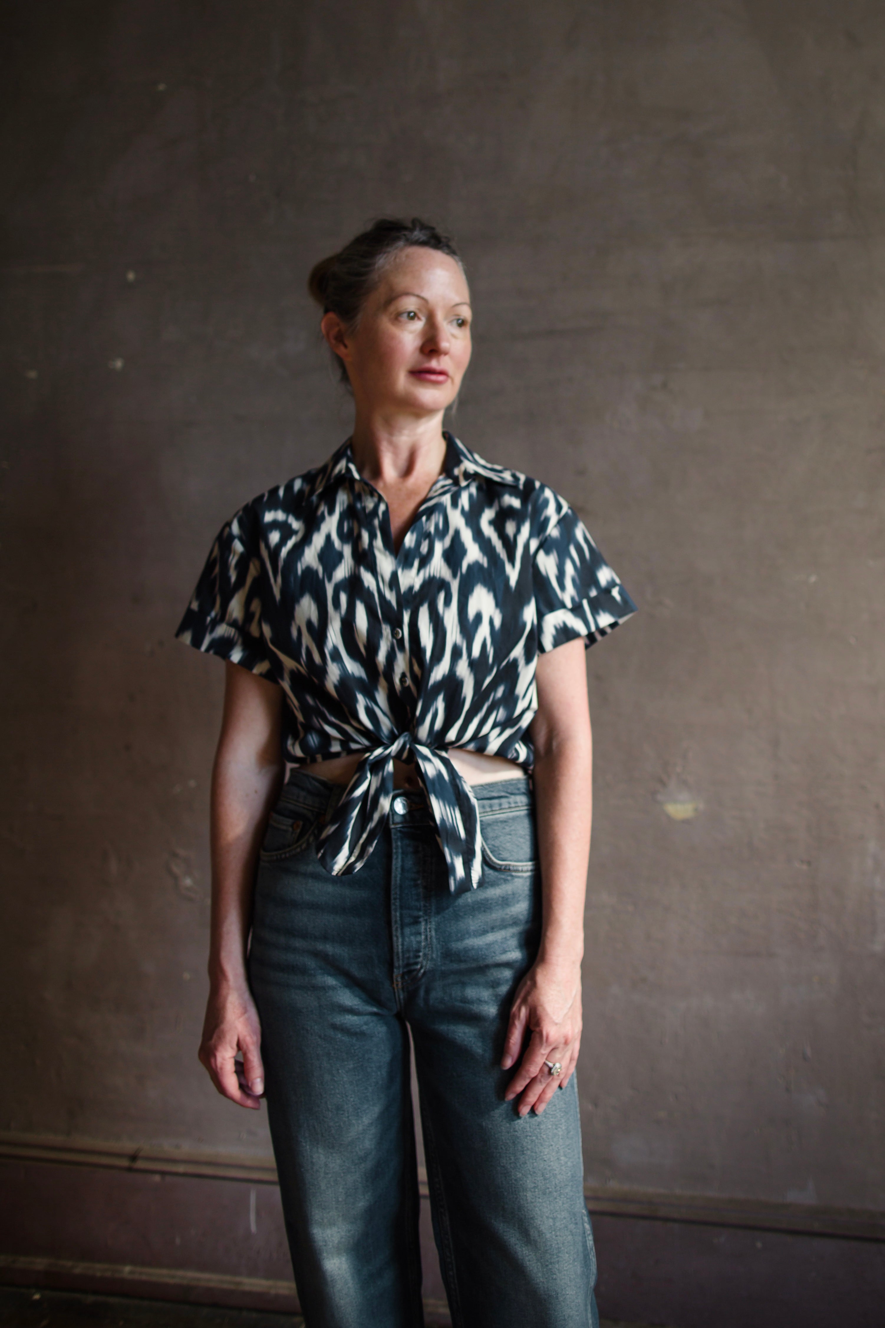 Image featuring a woman wearing the Asbury cropped shirtwith a button-down opening, cuffed short sleeve and a front tie bow detail and an elastic at back hem.