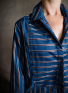 Image featuring a woman wearing the bib striped top by Cissa with a button front stripe placket and cropped, boxy fit in a blue and brown stripe.