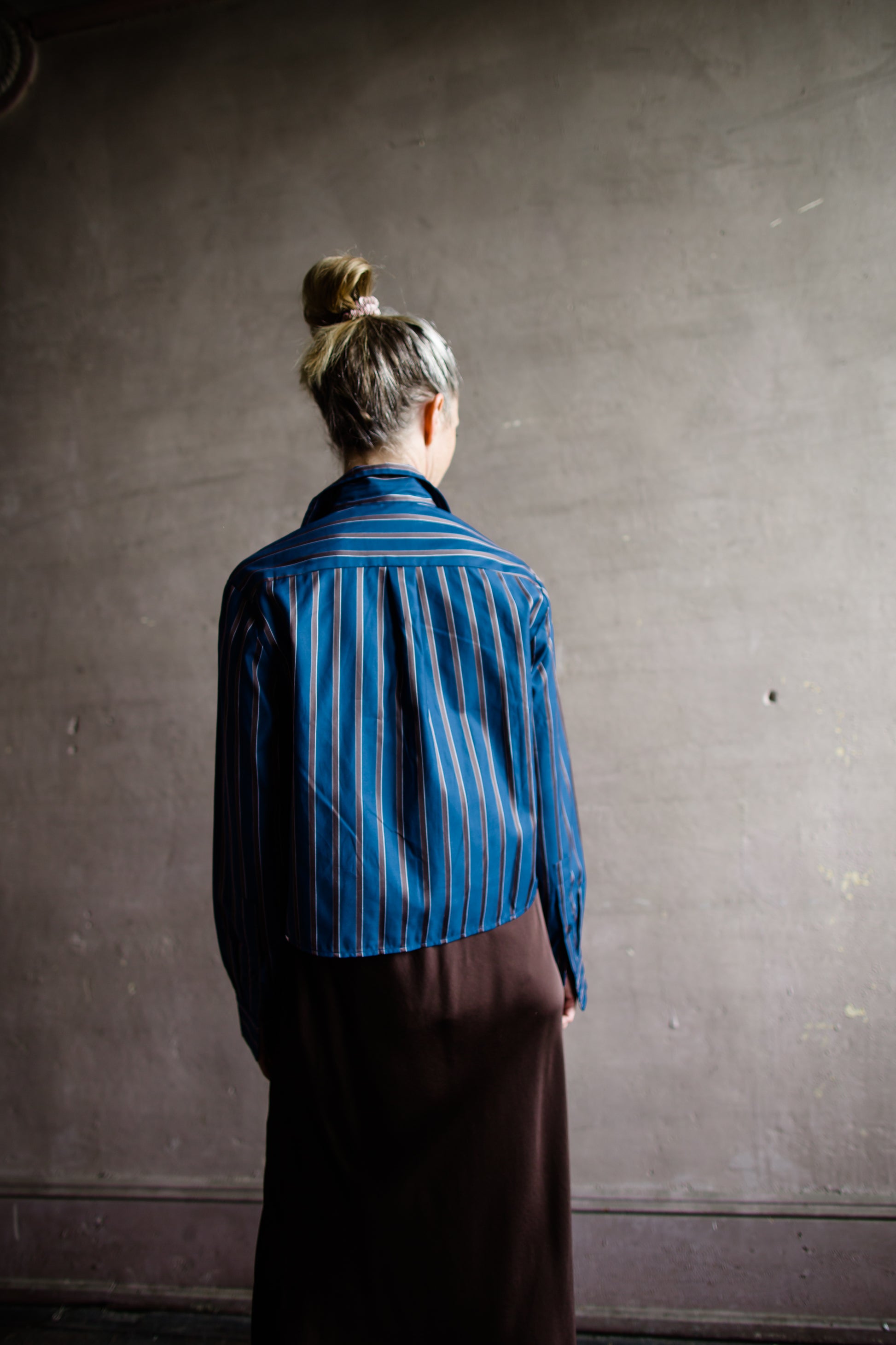 Image featuring a woman wearing the bib striped top by Cissa with a button front stripe placket and cropped, boxy fit in a blue and brown stripe.