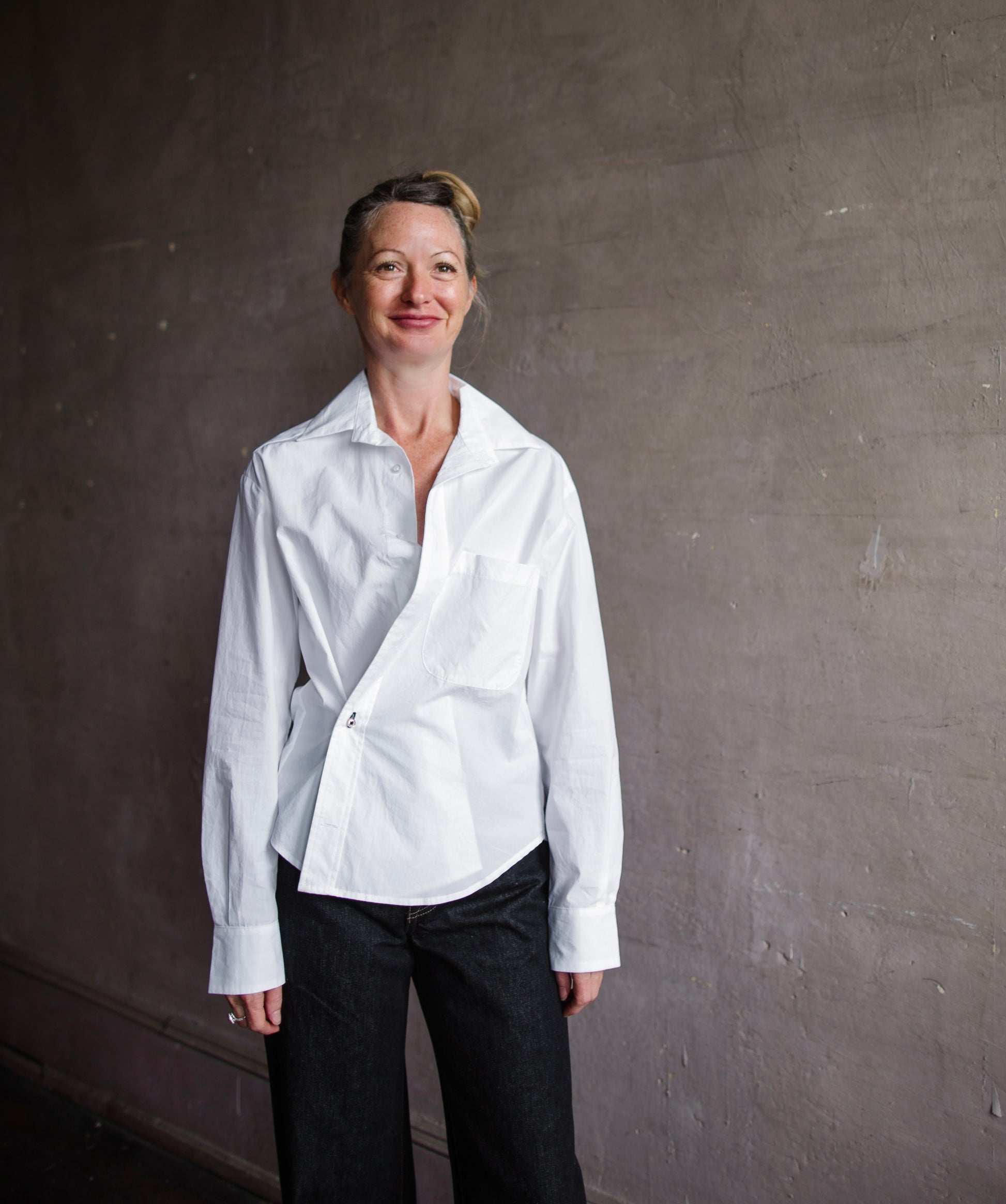 Image of a woman wearing the white cotton twist top by Cissa with a button front that can be worn multiple ways- buttoned across the waist or straight down.