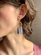 Woman wearing Delta Earrings from New York fine jewelry artist Emilie Shapiro with dangling teardrop shaped polished kyanite and warm textured half circle brass dangle gracefully from handmade gold filled earring wires