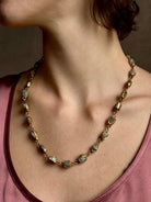 Woman wearing Guardian Path Necklace from jewelry designer Emilie Shapiro with posts on Natural emeralds individually embedded in warm brass along a clean, linear path for a beautiful statement piece handcrafted in USA