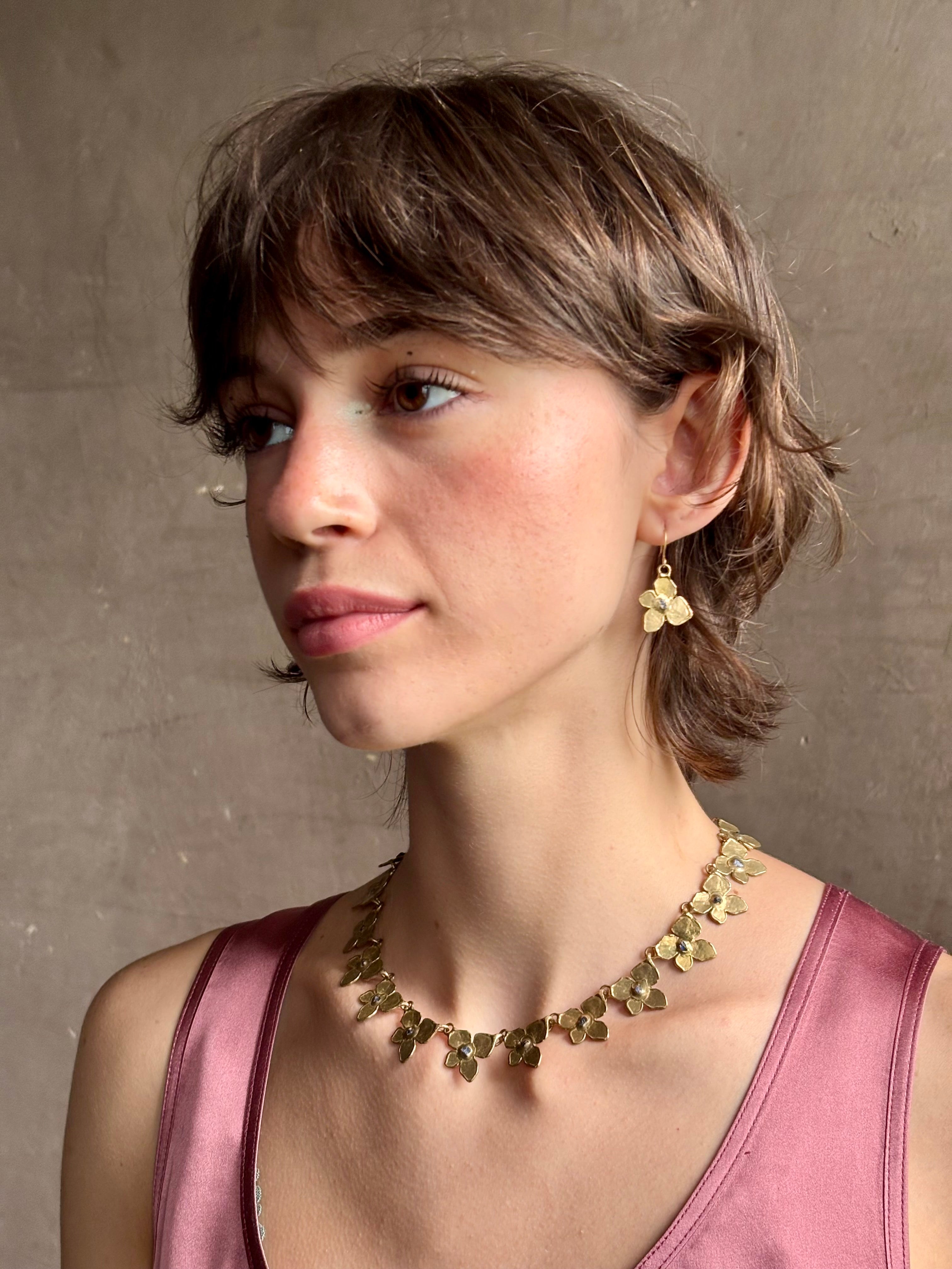 Woman wearing Hydrangea Collar Necklace from New Yok fine jewelry designer Emilie Shapiro is a statement  piece with Natural blue sapphires are individually embedded in warm, textured brass with artful exploration of form and movement handcrafted in USA