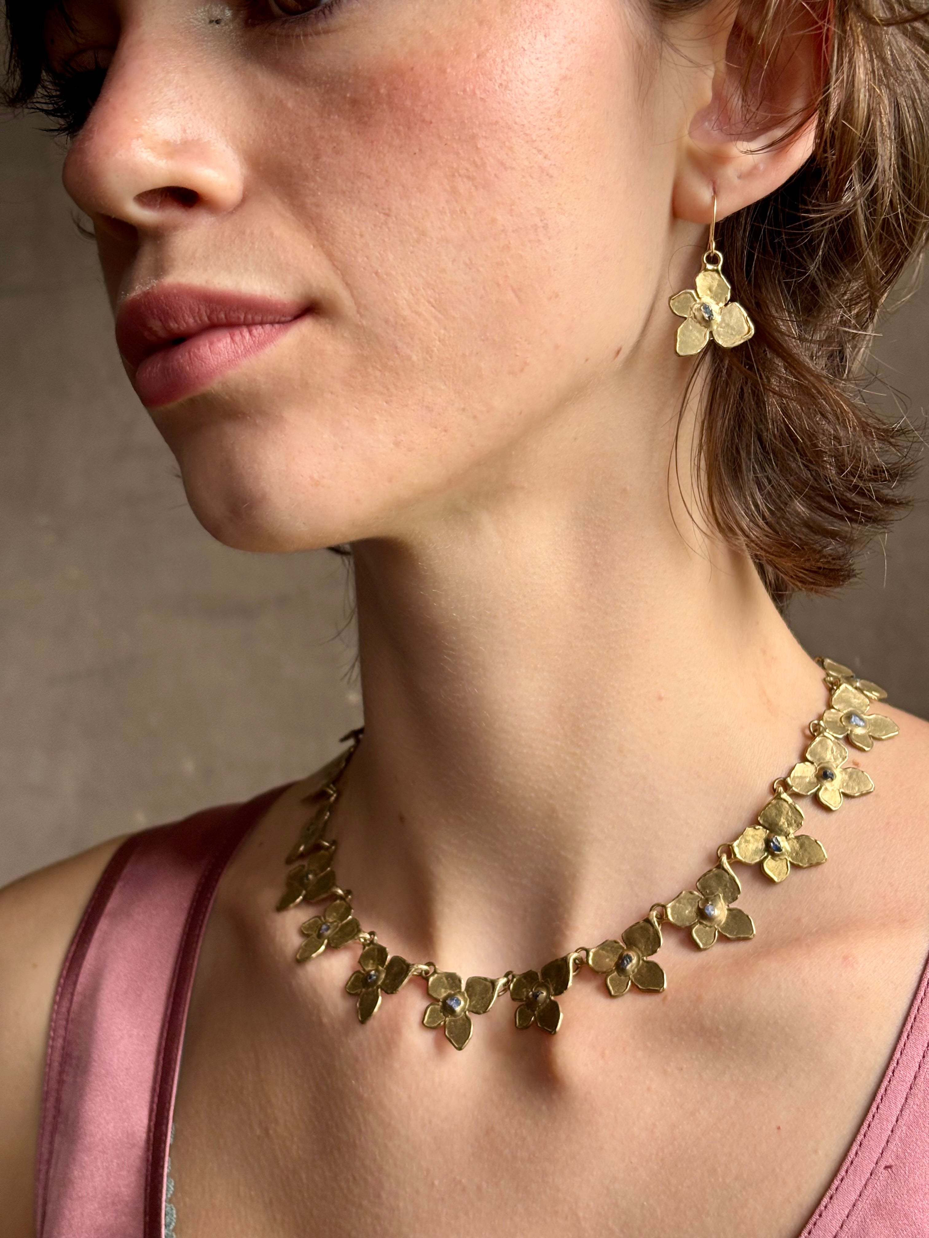 Woman wearing Hydrangea Collar Necklace from New Yok fine jewelry designer Emilie Shapiro is a statement  piece with Natural blue sapphires are individually embedded in warm, textured brass with artful exploration of form and movement handcrafted in USA