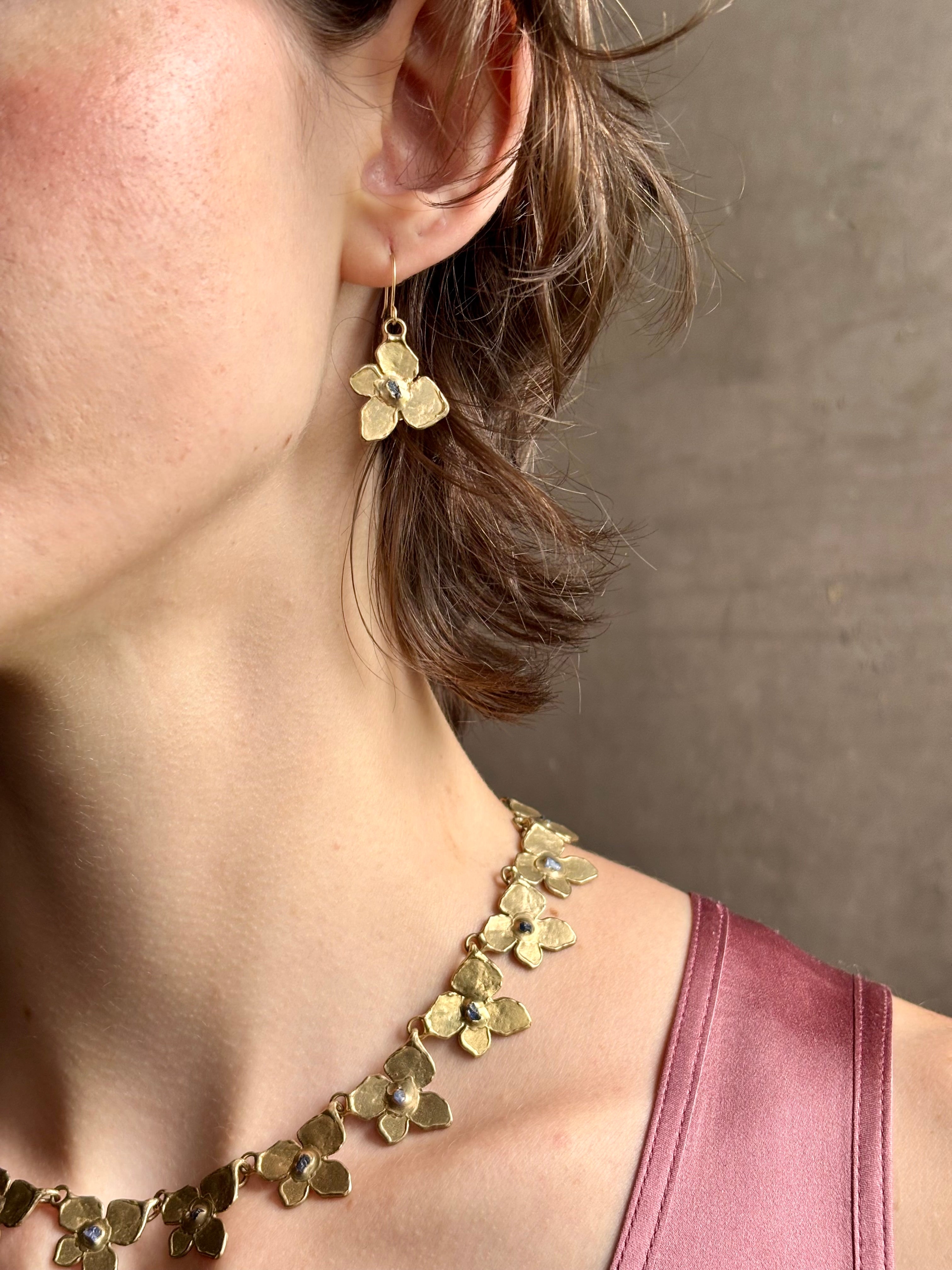 Woman wearing Hydrangea Earrings from New York fine jewelry artist Emilie Shapiro are botanically inspired with Raw sapphires embedded in warm, textured brass dangle from gold wire hoops handcrafted in USA