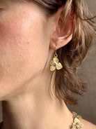 Woman wearing Hydrangea Earrings from New York fine jewelry artist Emilie Shapiro are botanically inspired with Raw sapphires embedded in warm, textured brass dangle from gold wire hoops handcrafted in USA