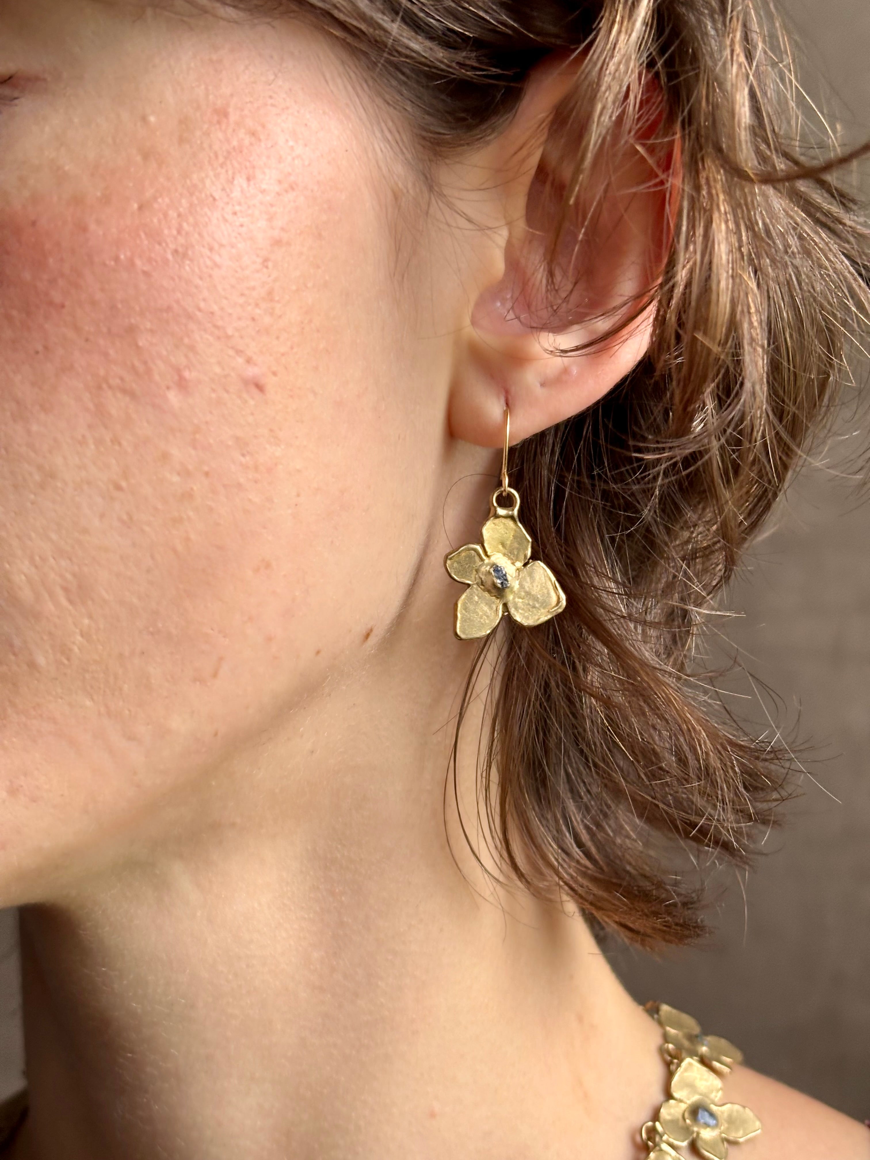 Woman wearing Hydrangea Earrings from New York fine jewelry artist Emilie Shapiro are botanically inspired with Raw sapphires embedded in warm, textured brass dangle from gold wire hoops handcrafted in USA