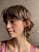 Woman wearing Lyra Earrings from designer jewelry artist Emilie Shapiro with iridescent paua shells dangling from textured brass and a gold filled wire hook with beautiful movement handcrafted in USA