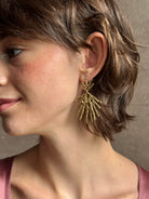 Woman wearing Solaris post Earrings from New York fine jewelry artist Emilie Shapiro that channels the radiant, life-giving energy of the sun in an exquisitely handcrafted textured brass form. Large, statement-making and thoroughly wearable dangle earrings