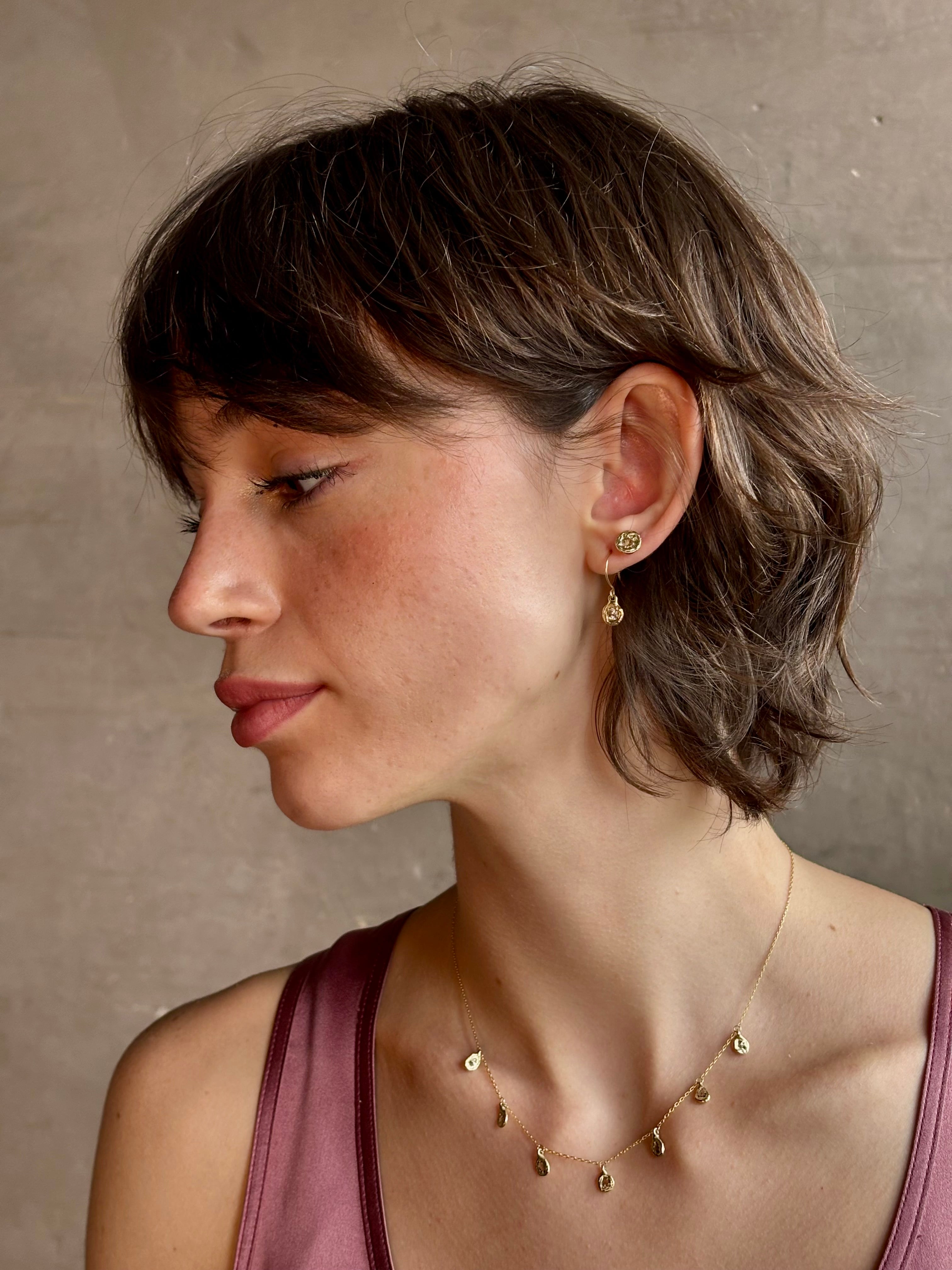 Woman wearing white Sapphire drop earrings from contemporary fine jewelry designer Emilie Shapiro composed of a single round white sapphires set in 14k yellow gold handcrafted in USA