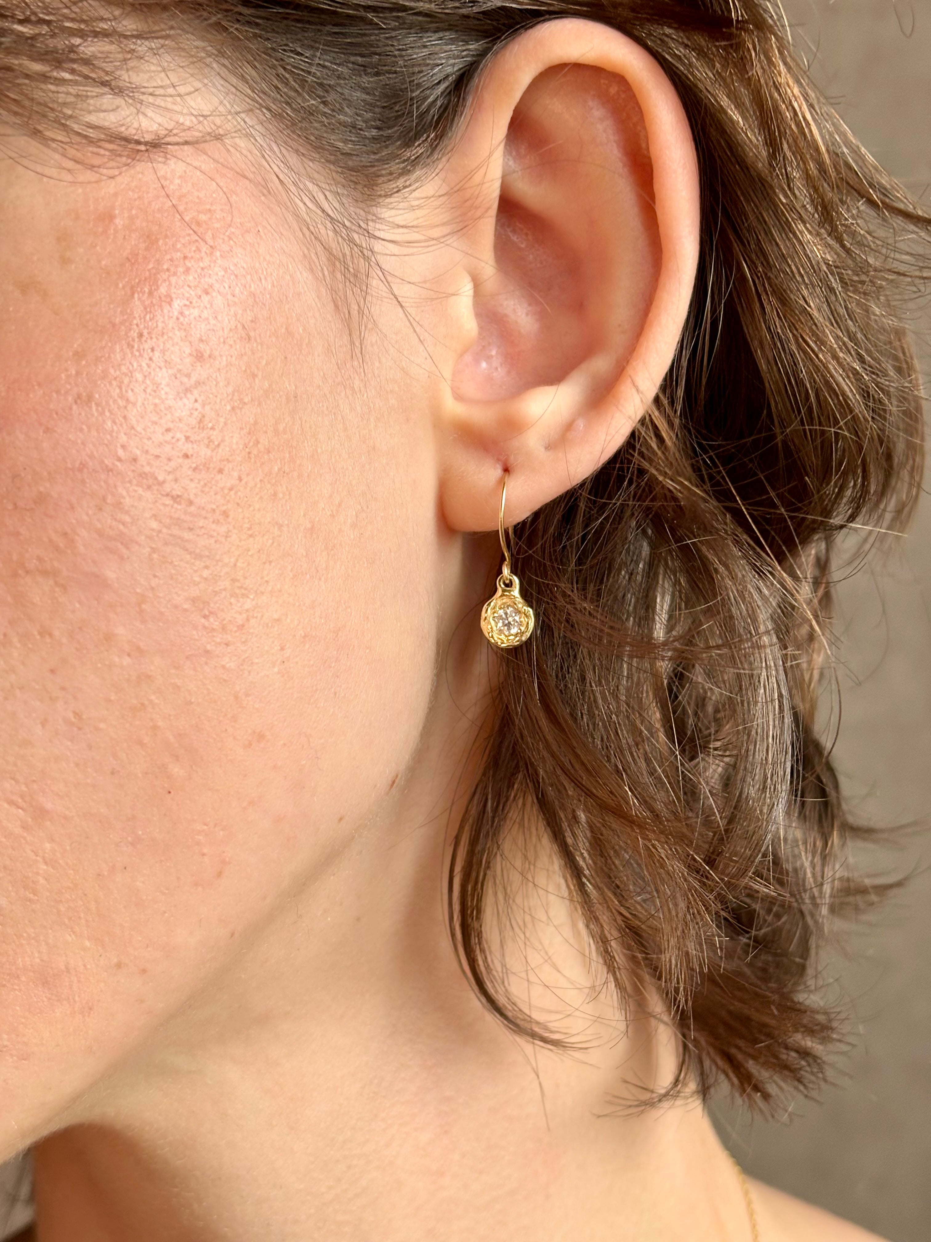 Woman wearing white Sapphire drop earrings from contemporary fine jewelry designer Emilie Shapiro composed of a single round white sapphires set in 14k yellow gold handcrafted in USA