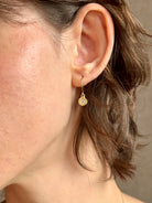 Woman wearing white Sapphire drop earrings from contemporary fine jewelry designer Emilie Shapiro composed of a single round white sapphires set in 14k yellow gold handcrafted in USA