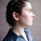 Woman wearing hand hammered sterling silver pentagon frames lined with rubies lining dangling from wire hooks by Erica Bailey
