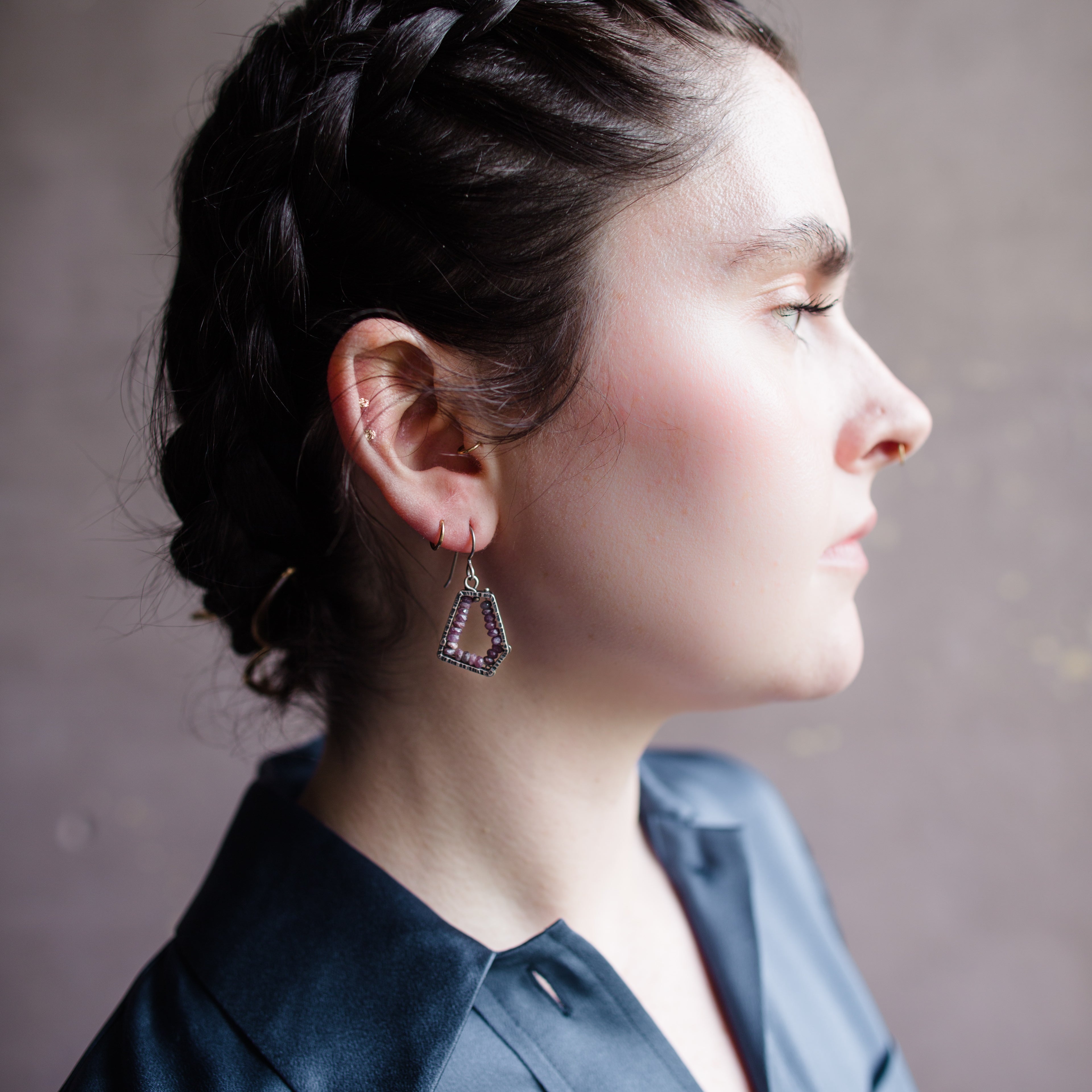 Woman wearing hand hammered sterling silver pentagon frames lined with rubies lining dangling from wire hooks by Erica Bailey