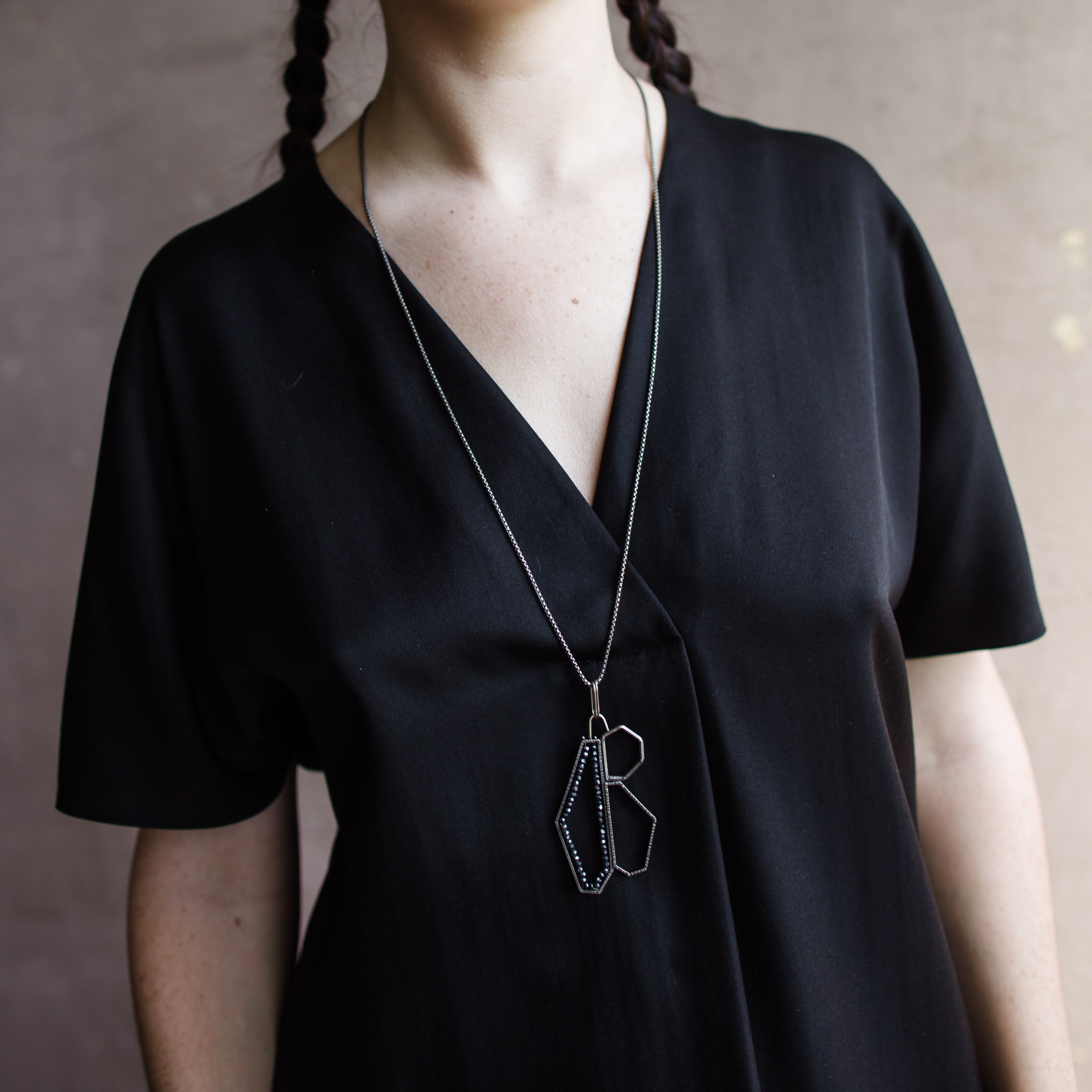 Woman wearing a black top and showcasing a sterling silver and spinel pendant necklace with a geometric design by North Carolina jewelry artist Erica Bailey